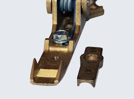 Zbliżenie na metalową stopę dociskową maszyny do szycia i małą, odłączoną metalową część na zwykłym tle.