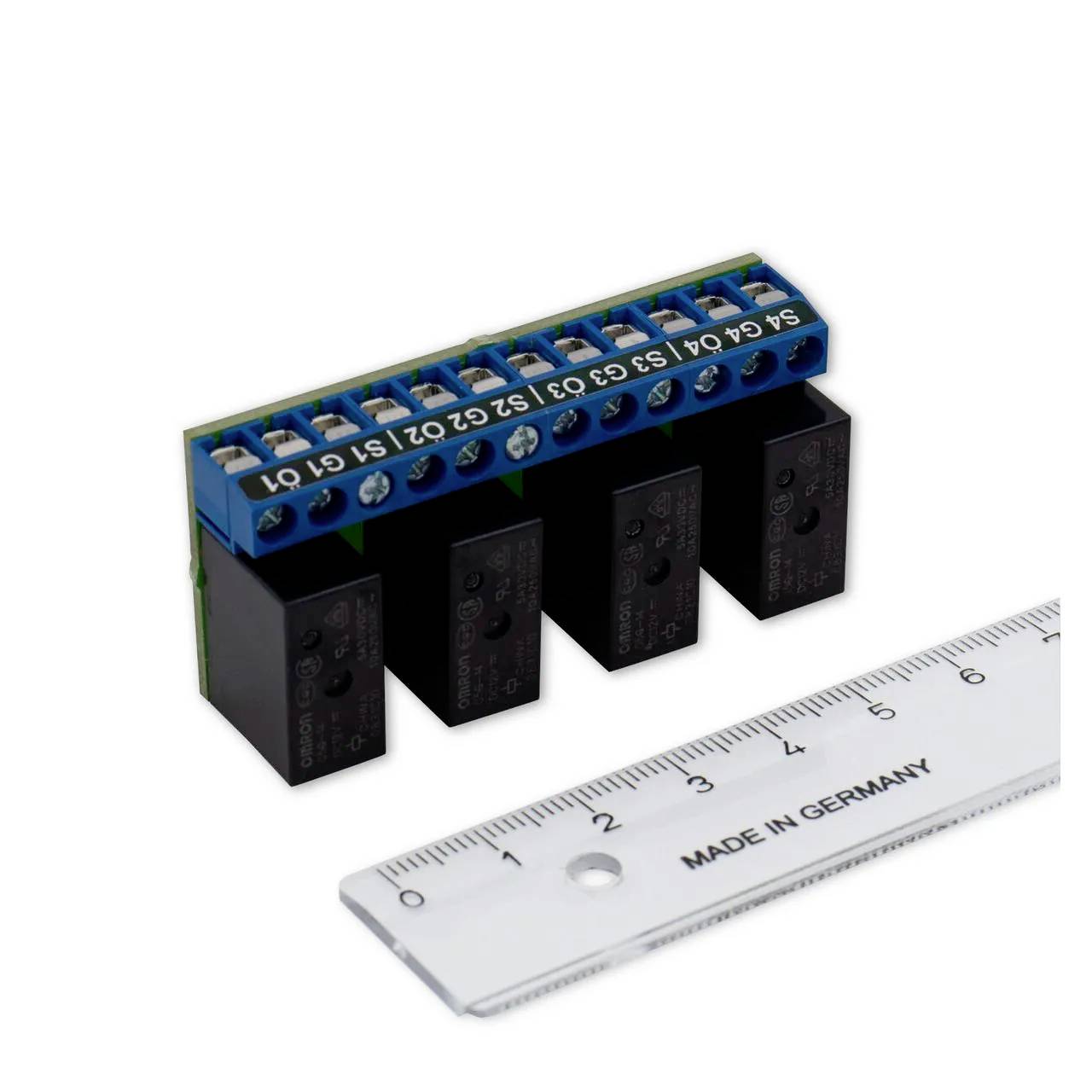 Niebieski blok zaciskowy z podłączonymi elementami przewodowymi i czterema czarnymi przekaźnikami. Obok niego leży przezroczysta linijka, oznaczona w centymetrach.