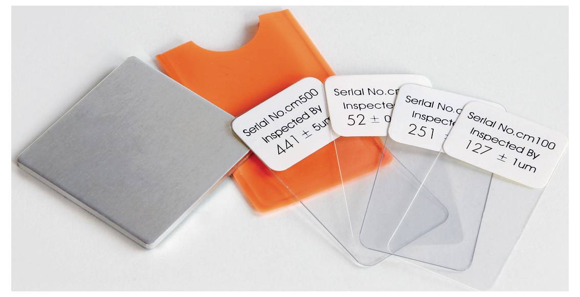 'Trzy kartonowe etykiety z numerami seryjnymi i informacjami z inspekcji na przezroczystych płytach z tworzywa sztucznego, wraz z pomarańczowym etui.'