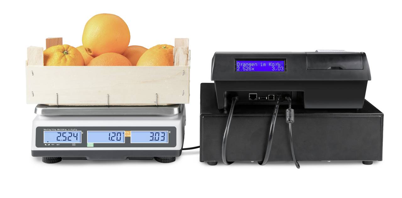Skrzynia z pomarańczami jest ważona na wadze cyfrowej, podłączonej do systemu kasowego, który wyświetla cenę za kilogram.