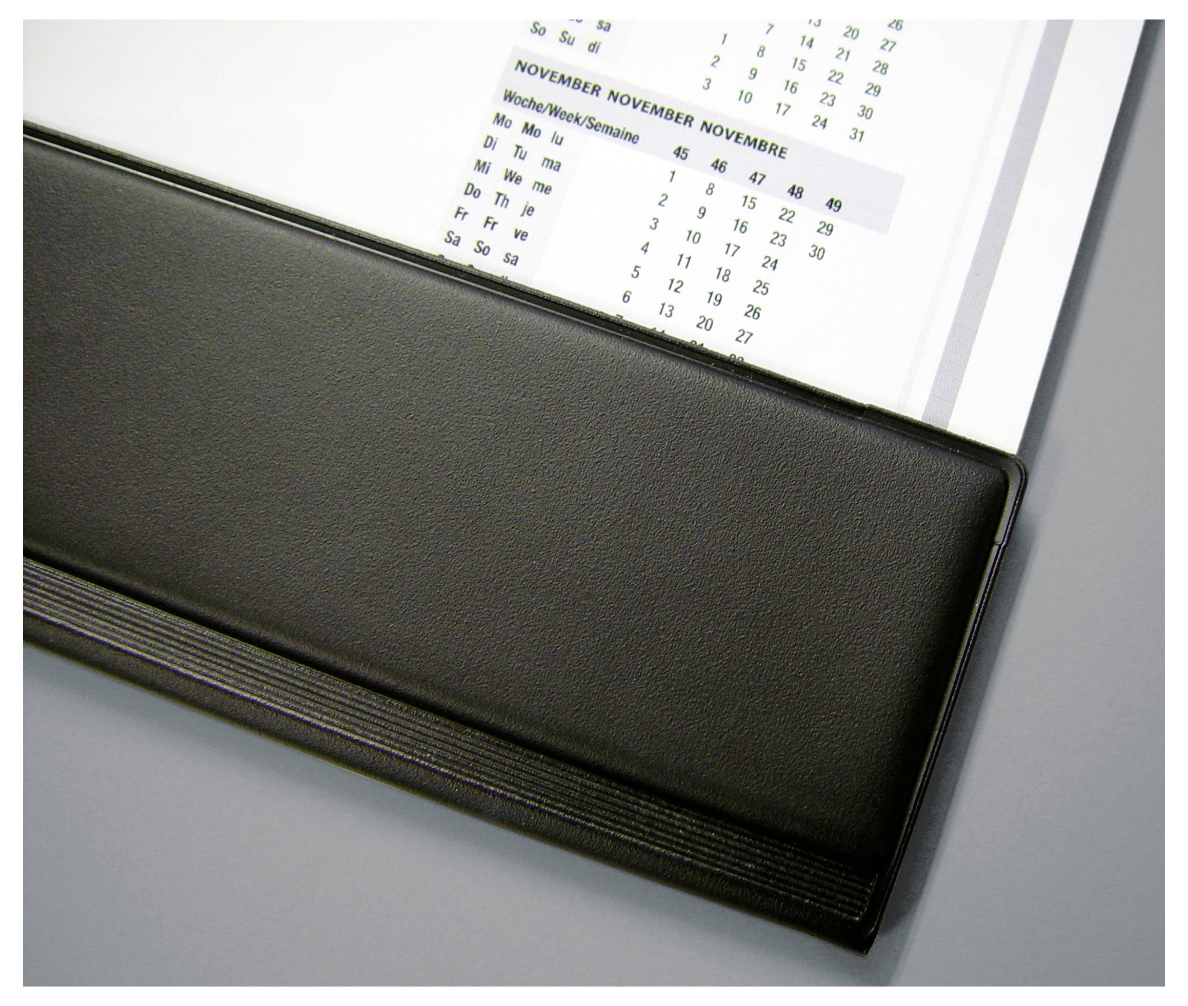 Kalendarz w czarnej skórzanej okładce na dolnym marginesie; przedstawia miesiąc listopad z wyróżnionymi dniami tygodnia.