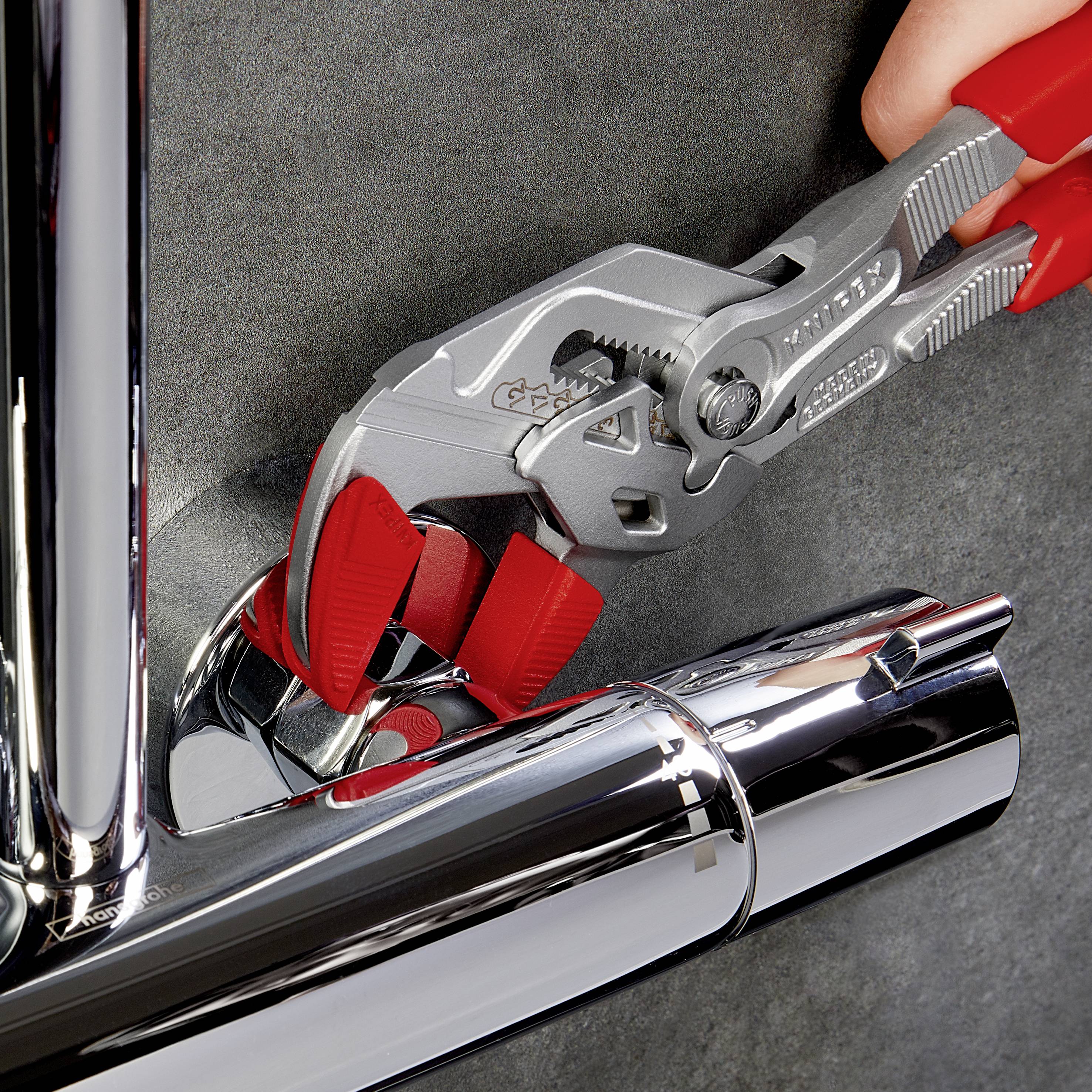 'Jedna ręka trzyma szczypce, które obejmują srebrną wylewkę. Szczypce mają czerwone gumowe uchwyty i są używane do konserwacji.'