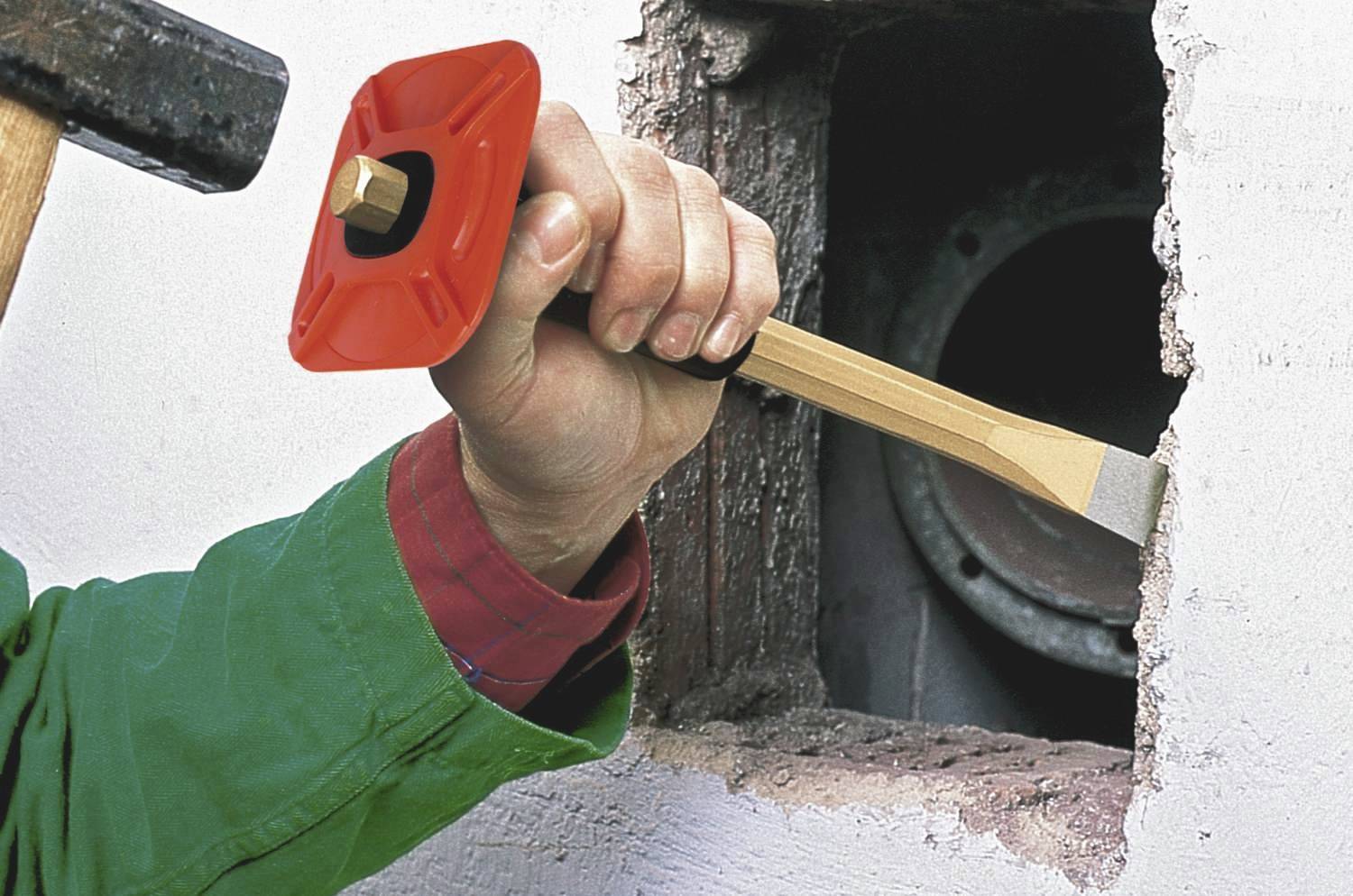 Rzemieślnik powiększa otwór w ścianie za pomocą dłuta i młotka.