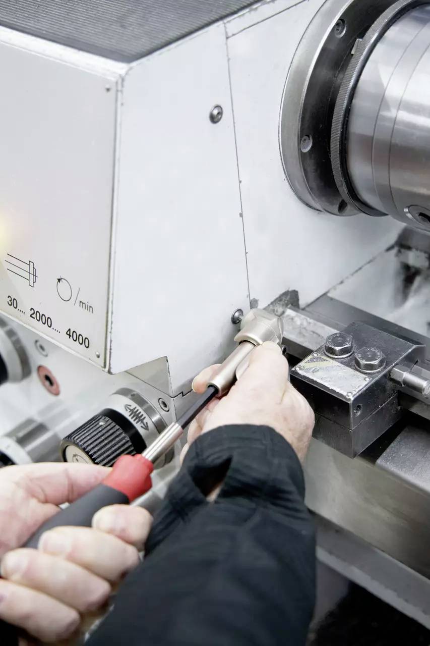 Osoba regulująca tokarkę metalową, koncentrująca się na sterownikach, wskazująca na czynność ustawienia lub konserwacji, z precyzyjną ręczną obsługą.