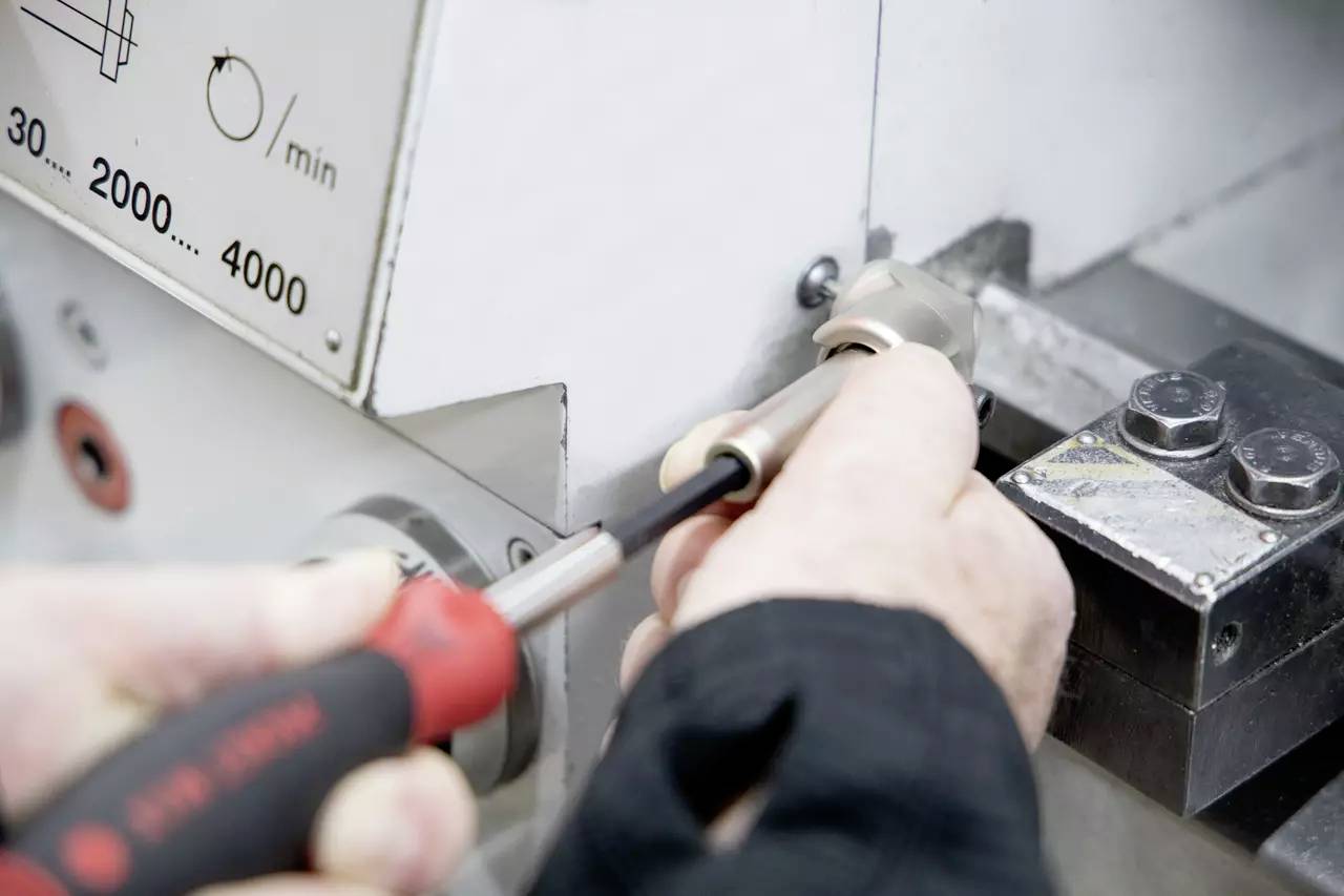 Osoba dokręca śrubę w maszynie za pomocą śrubokręta, koncentrując się na precyzyjnym ustawieniu urządzenia mechanicznego.