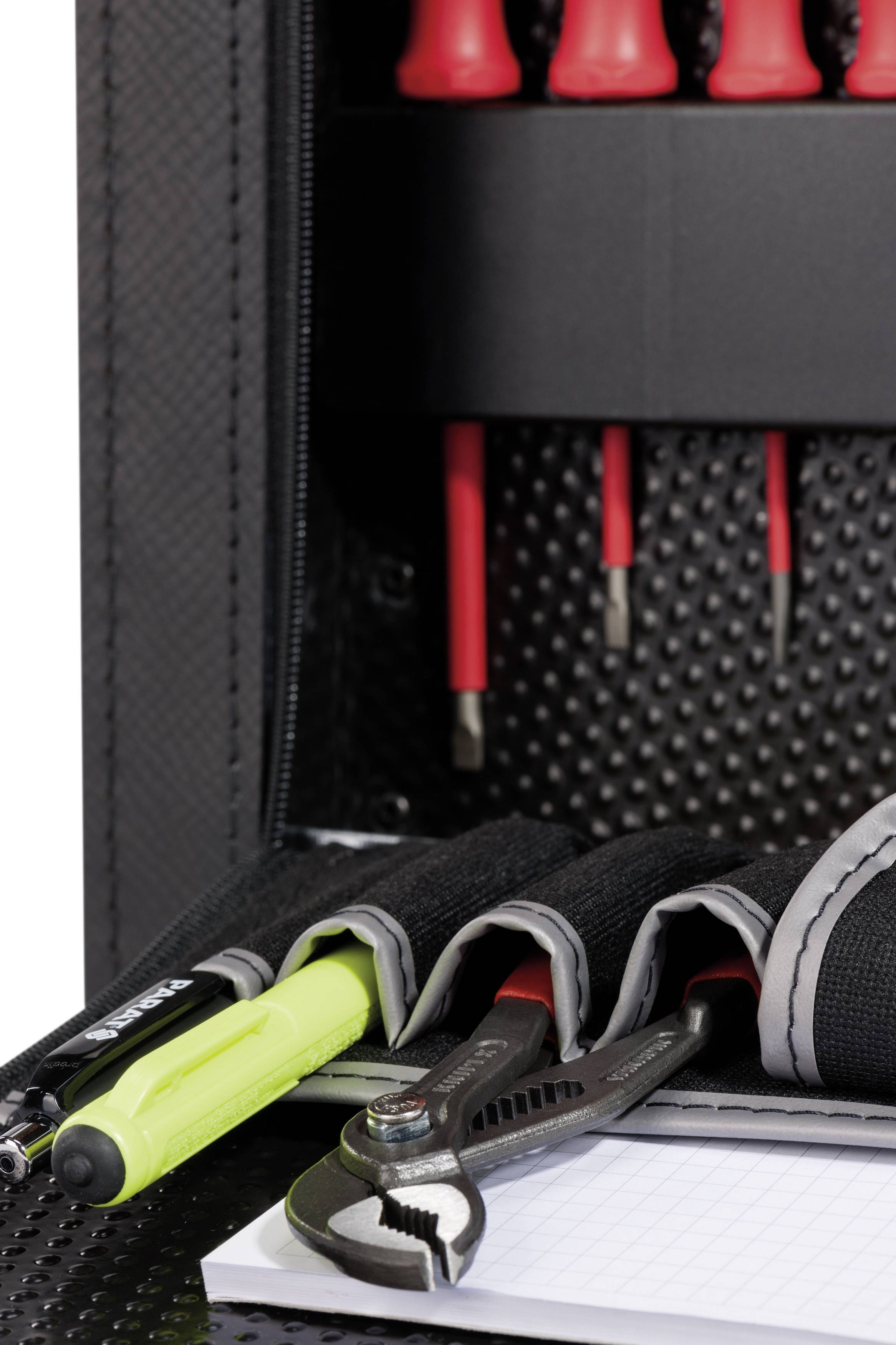 Otwarty kufer z narzędziami z różnymi przyborami, w tym śrubokręty, zielony długopis i szczypce na notatniku.