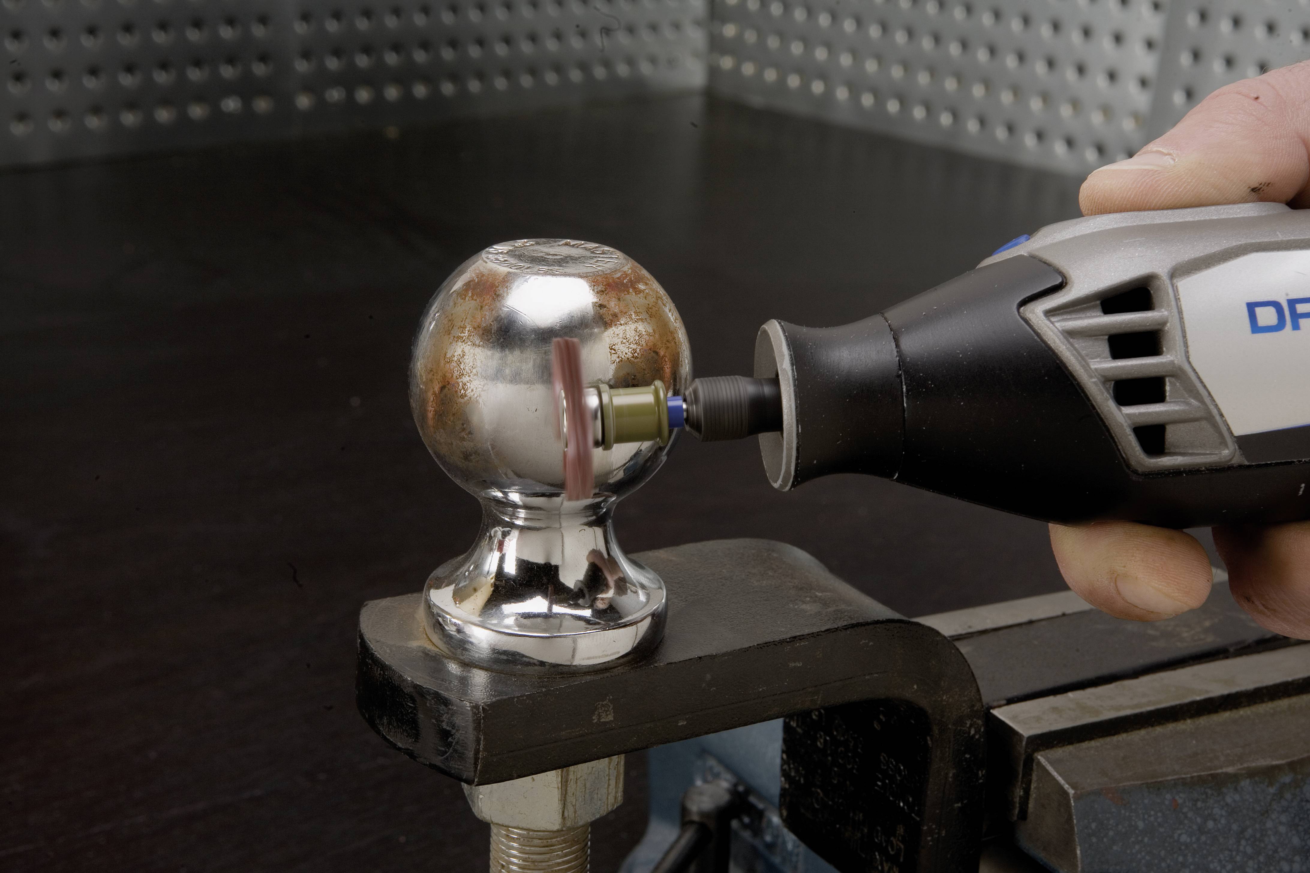 Jedna osoba poleruje metalową kulę obrotowym narzędziem, aby usunąć rdzę. Kula jest zamocowana w uchwycie.