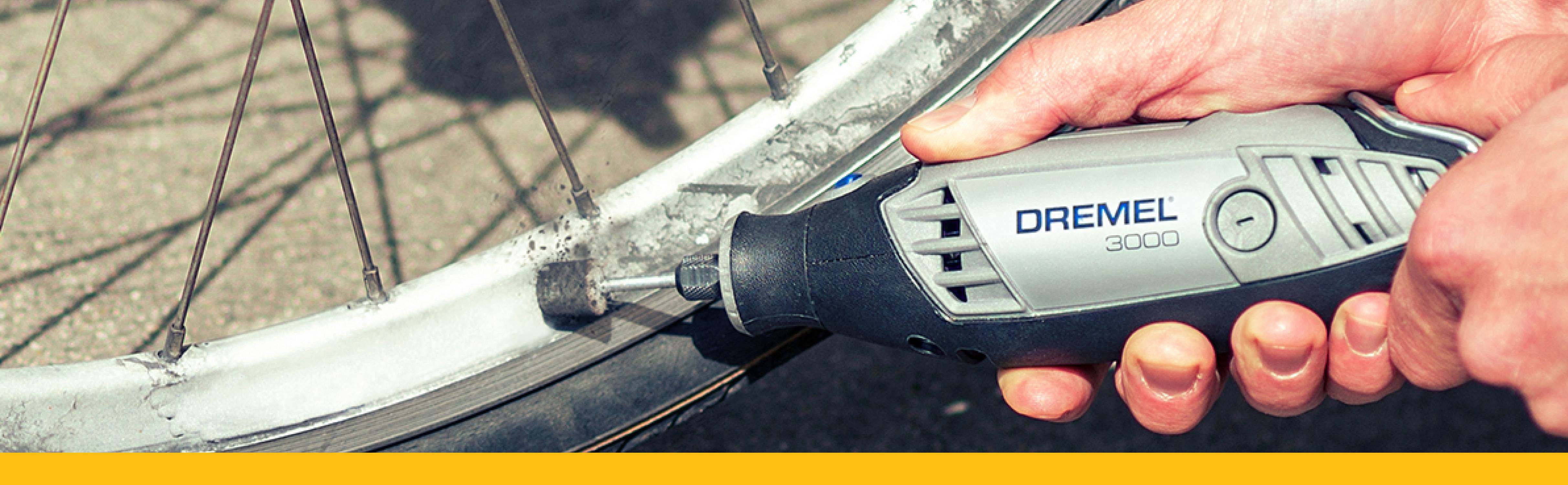 Jedna ręka trzyma narzędzie Dremel, które jest używane do szlifowania obręczy roweru. Nacisk położony jest na precyzyjnym procesie pracy.