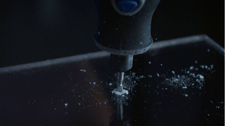 Zbliżenie wiertła wykonującego otwór w ciemnej powierzchni, otoczone odłamkami.