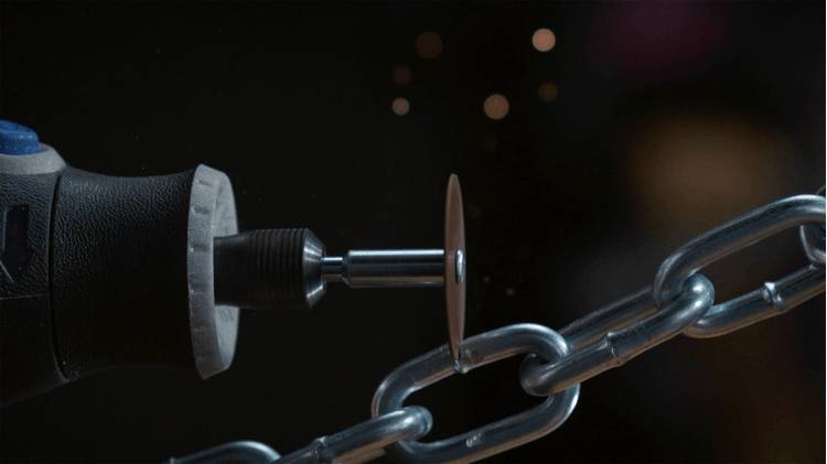 Zbliżenie narzędzia obrotowego z tarczą tnącą, która przecina metalowy łańcuch, na ciemnym tle z lecącymi iskrami.