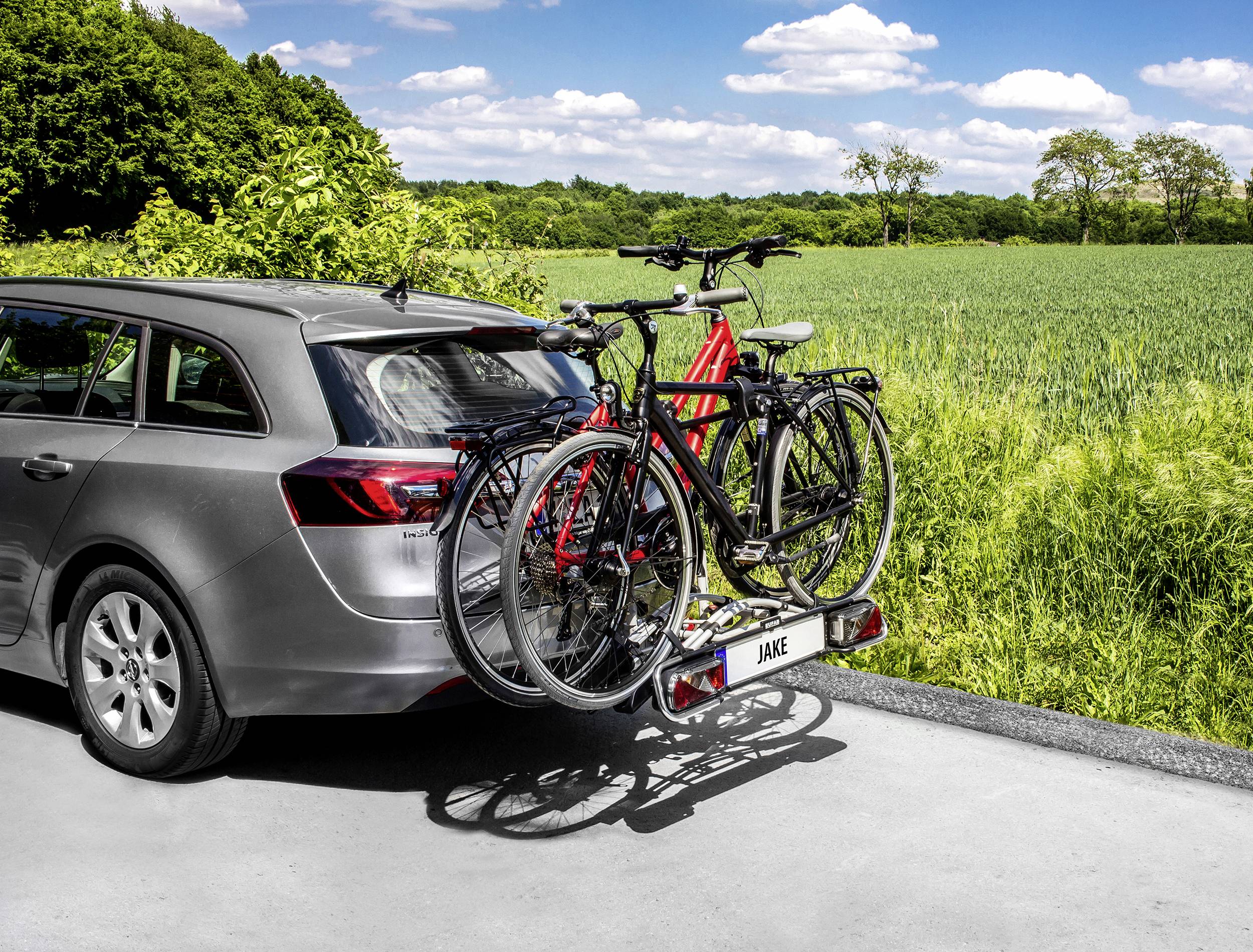 Szary samochód stoi na drodze, a na tylnym bagażniku zamocowane są dwa rowery. W tle widać zielone pola.