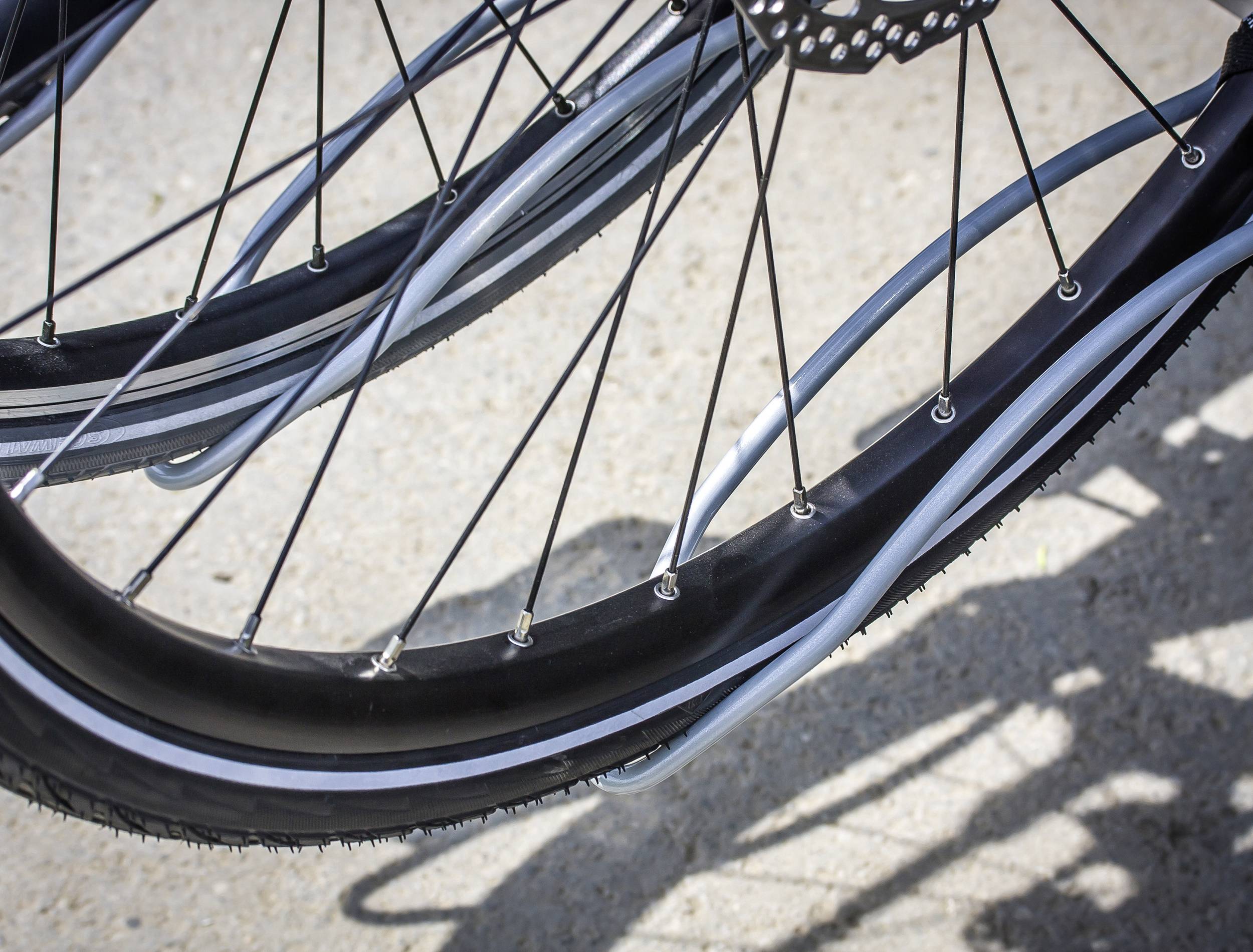 Zbliżenie dwóch opon rowerowych z czarnymi felgami i białymi szprychami na jasnej nawierzchni drogi.