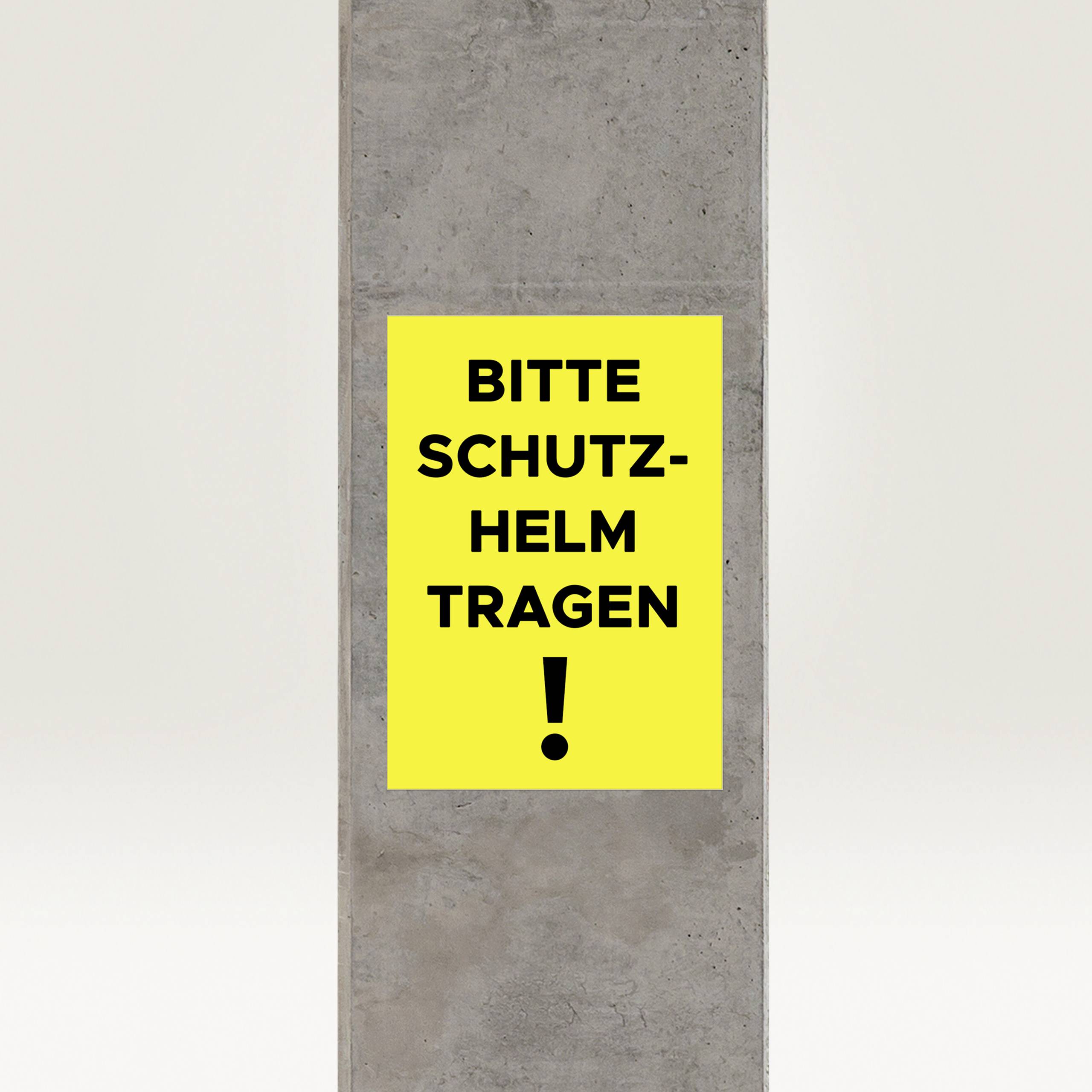 Betonowy słup z żółtą tabliczką i czarnym tekstem 'PROSZĘ NOSIĆ KASK OCHRONNY!', ważna informacja dotycząca bezpieczeństwa.