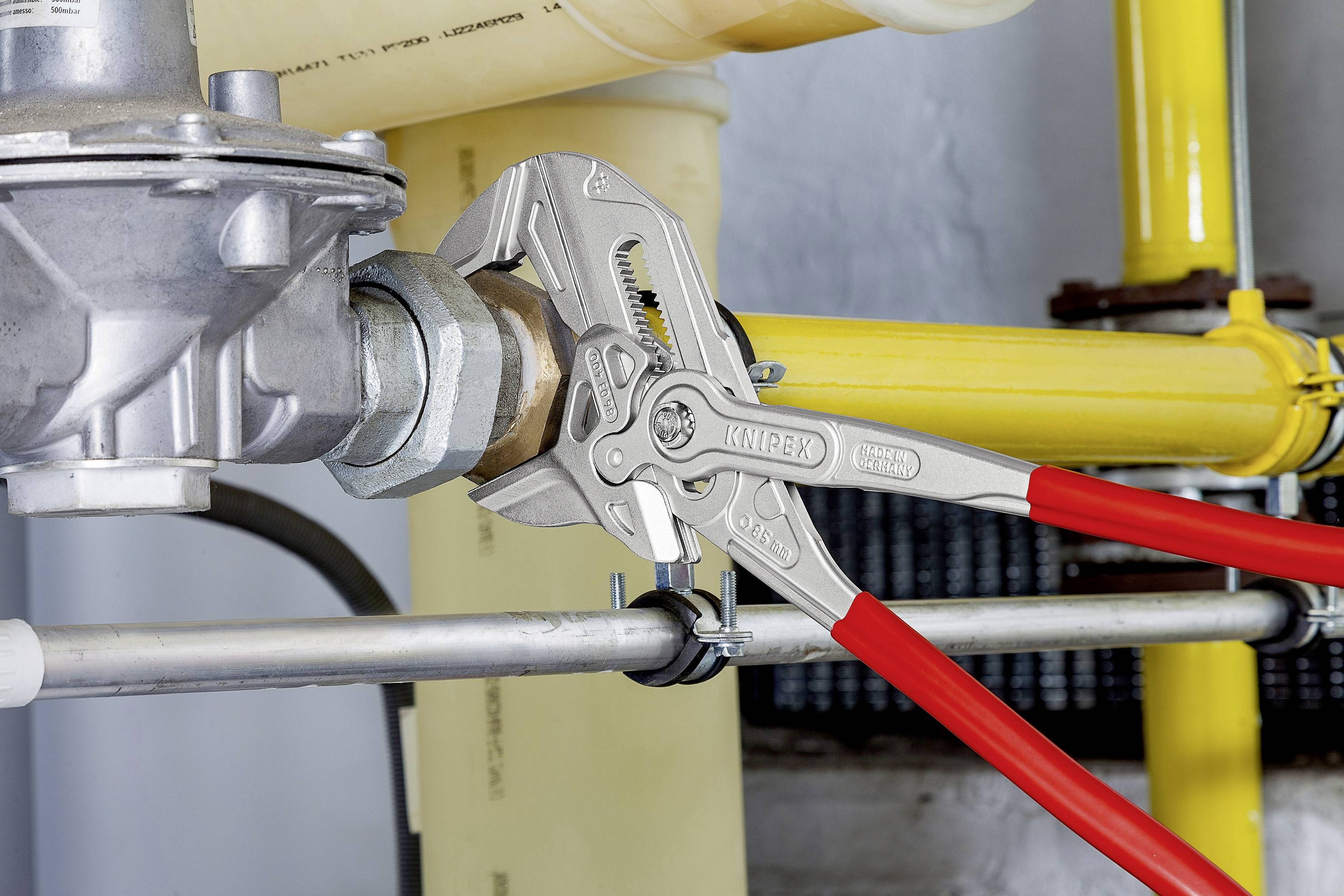 Szczypce z czerwonymi uchwytami są używane do zamocowania nakrętki metalowej na żółtej rurze.