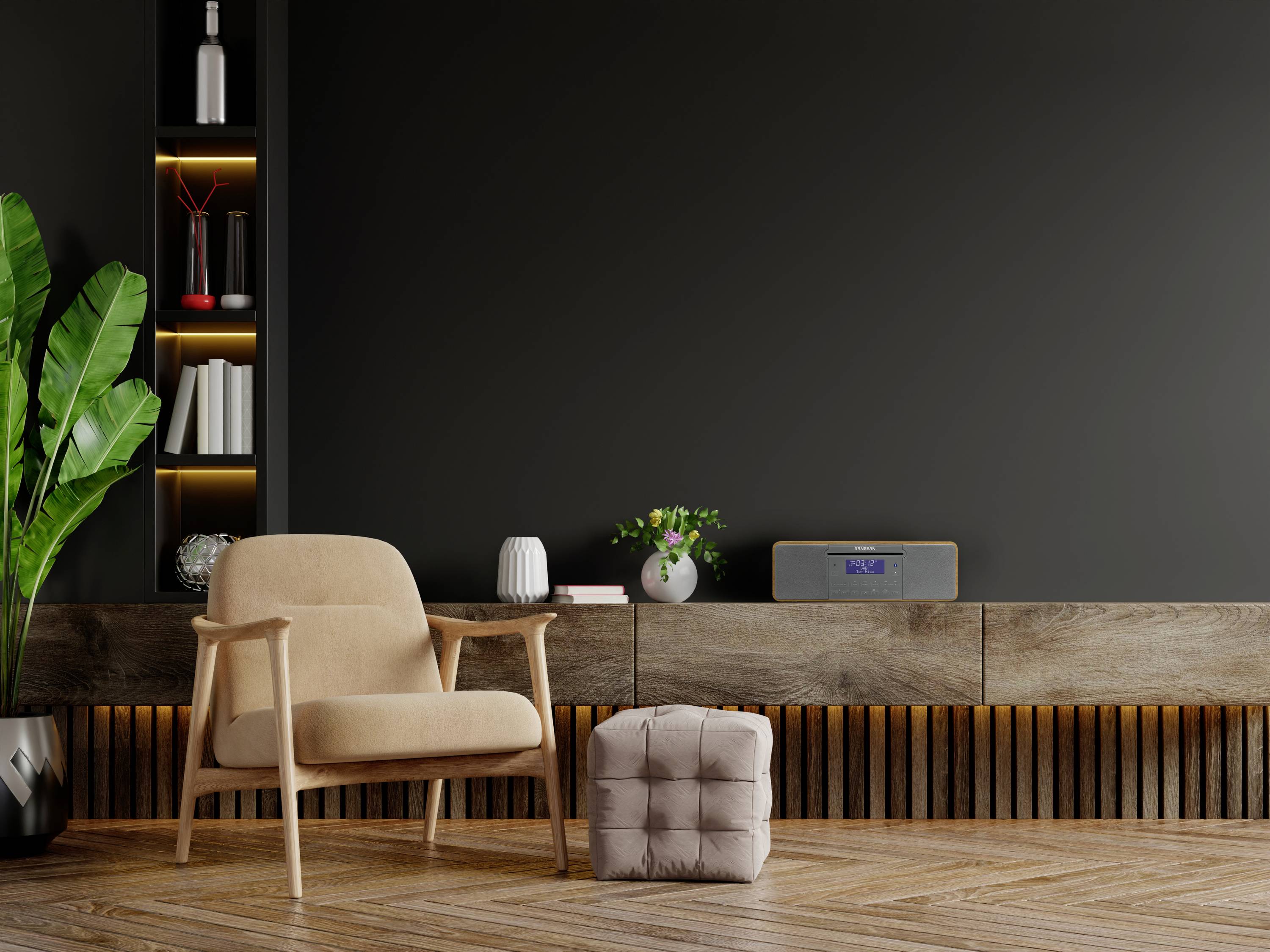 Jasny fotel stoi w nowoczesnym salonie przed ciemną ścianą, z kompozycją roślinną i niską drewnianą półką.