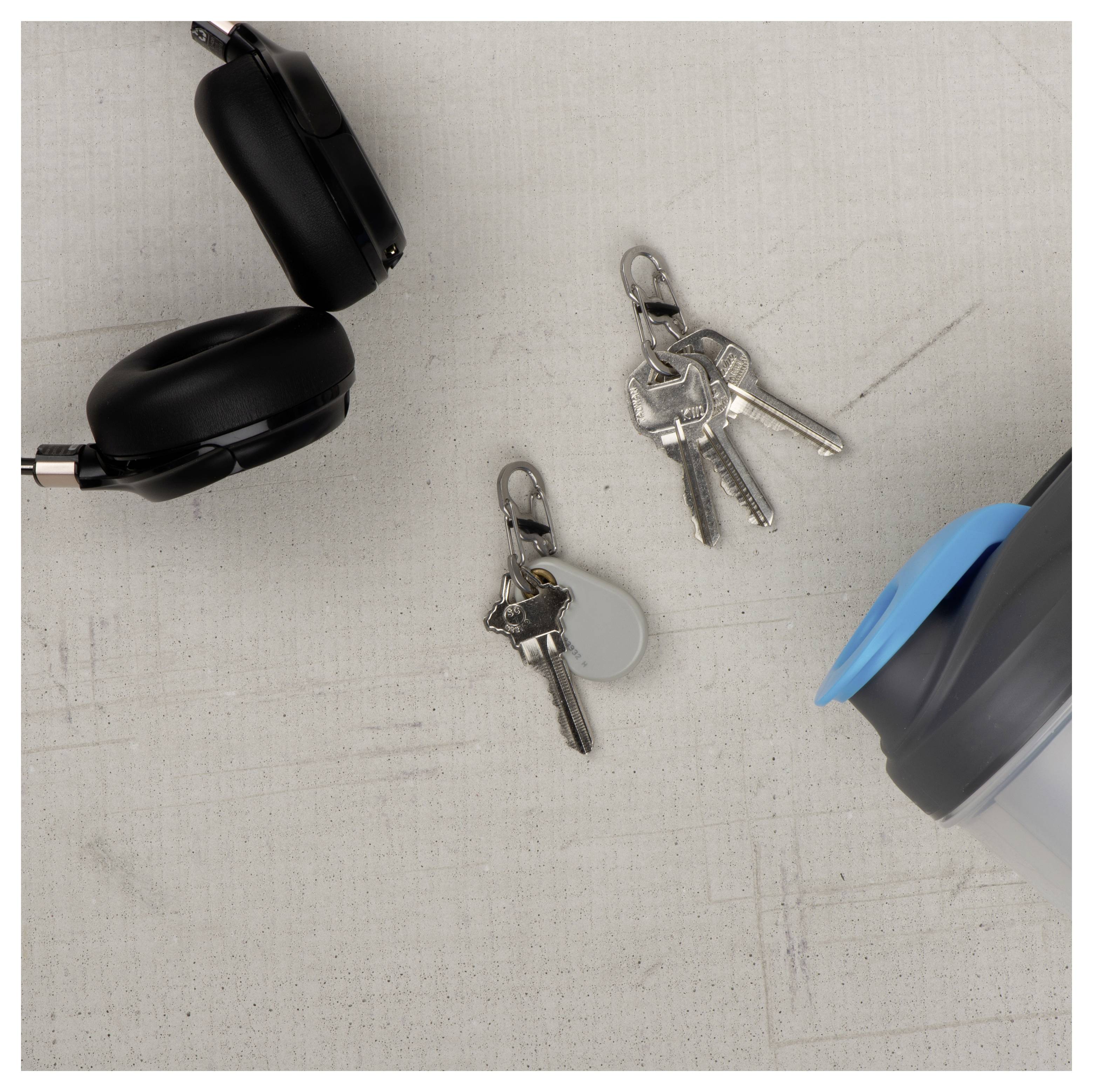 Bezprzewodowe słuchawki douszne, shaker oraz dwa komplety kluczy na jasnoszarej powierzchni.