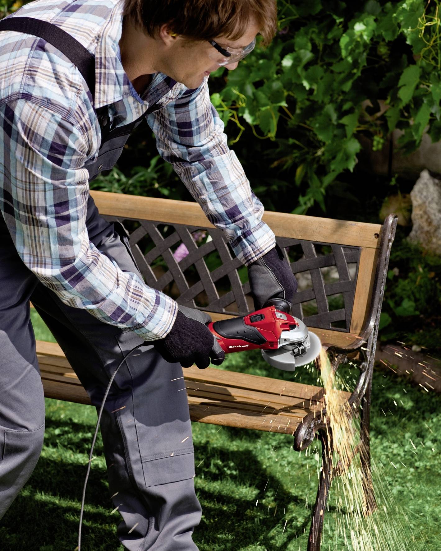 Osoba używa szlifierki kątowej do cięcia metalowego przedmiotu na wolnym powietrzu. Od tarczy szlifierskiej lecą iskry.