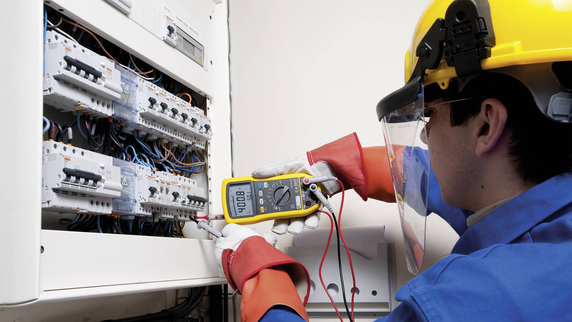 Technik w kasku ochronnym sprawdza skrzynkę elektryczną za pomocą multimetru.