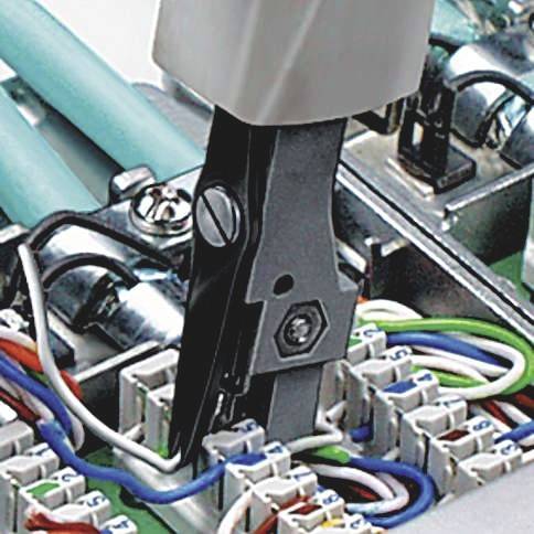 Zbliżenie narzędzia do cięcia przewodów w rozdzielnicy elektrycznej, z wieloma kablami i złączkami.