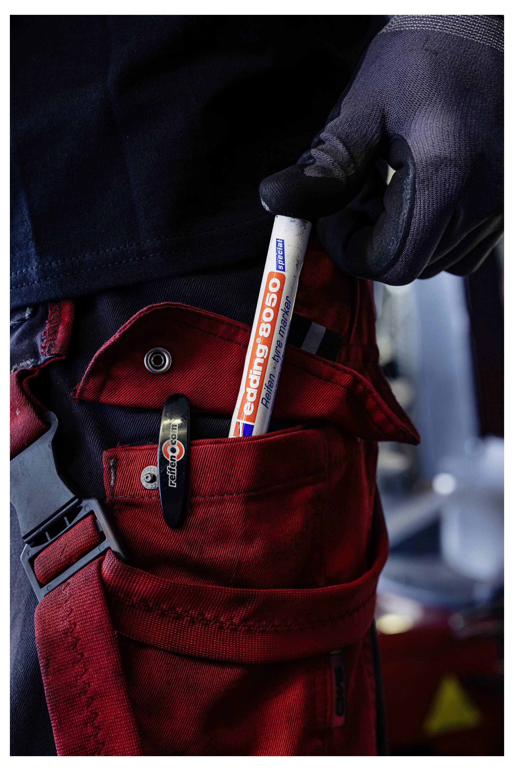 Dłoń w rękawiczce trzymająca marker "coling 8050" nad otwartą czerwoną torbą narzędziową ze sprzączką i kieszenią na zatrzask.