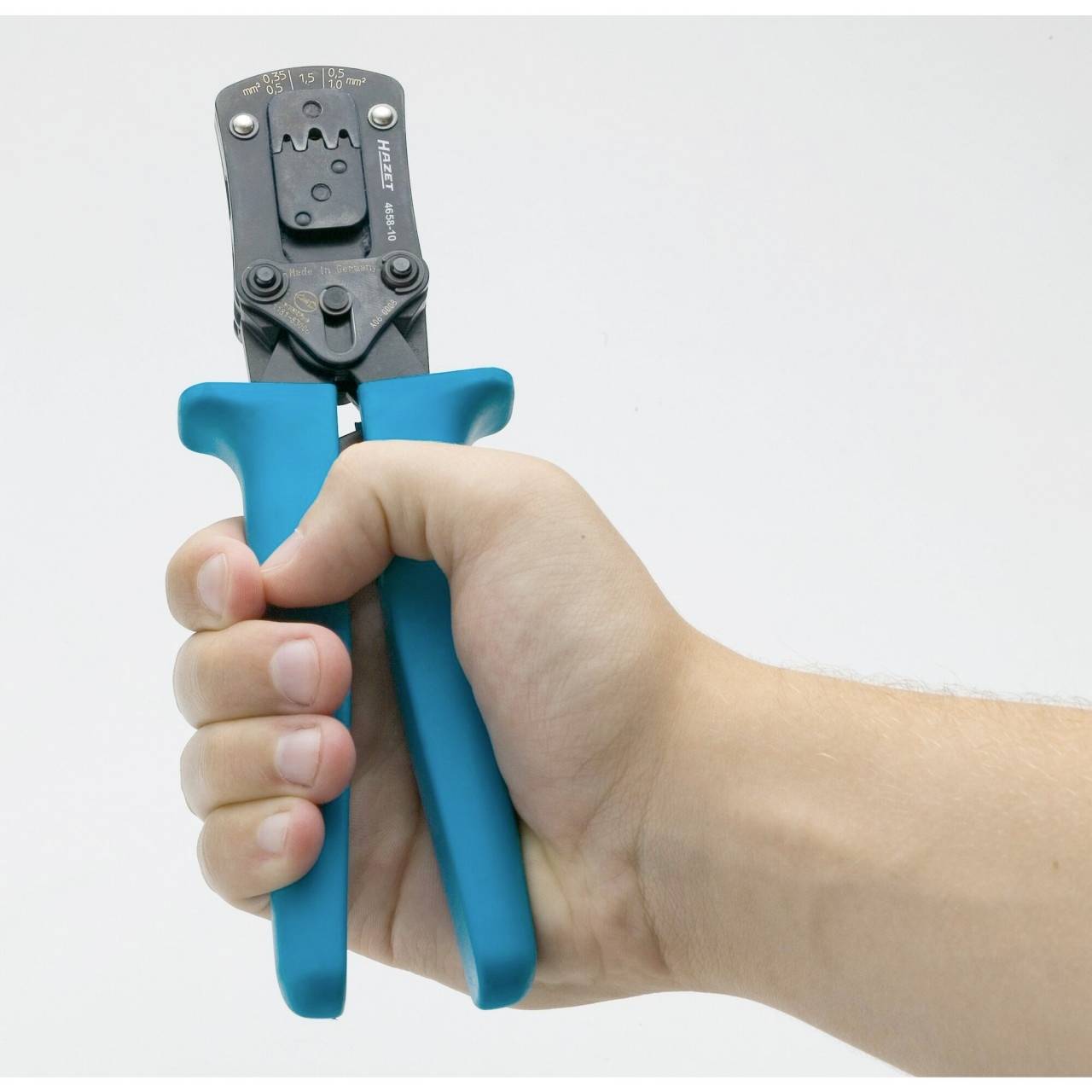 Dłoń trzyma szczypce zaciskowe z niebieskimi uchwytami. Szczypce są używane do połączeń kablowych i są mocno ściskane w ręku.