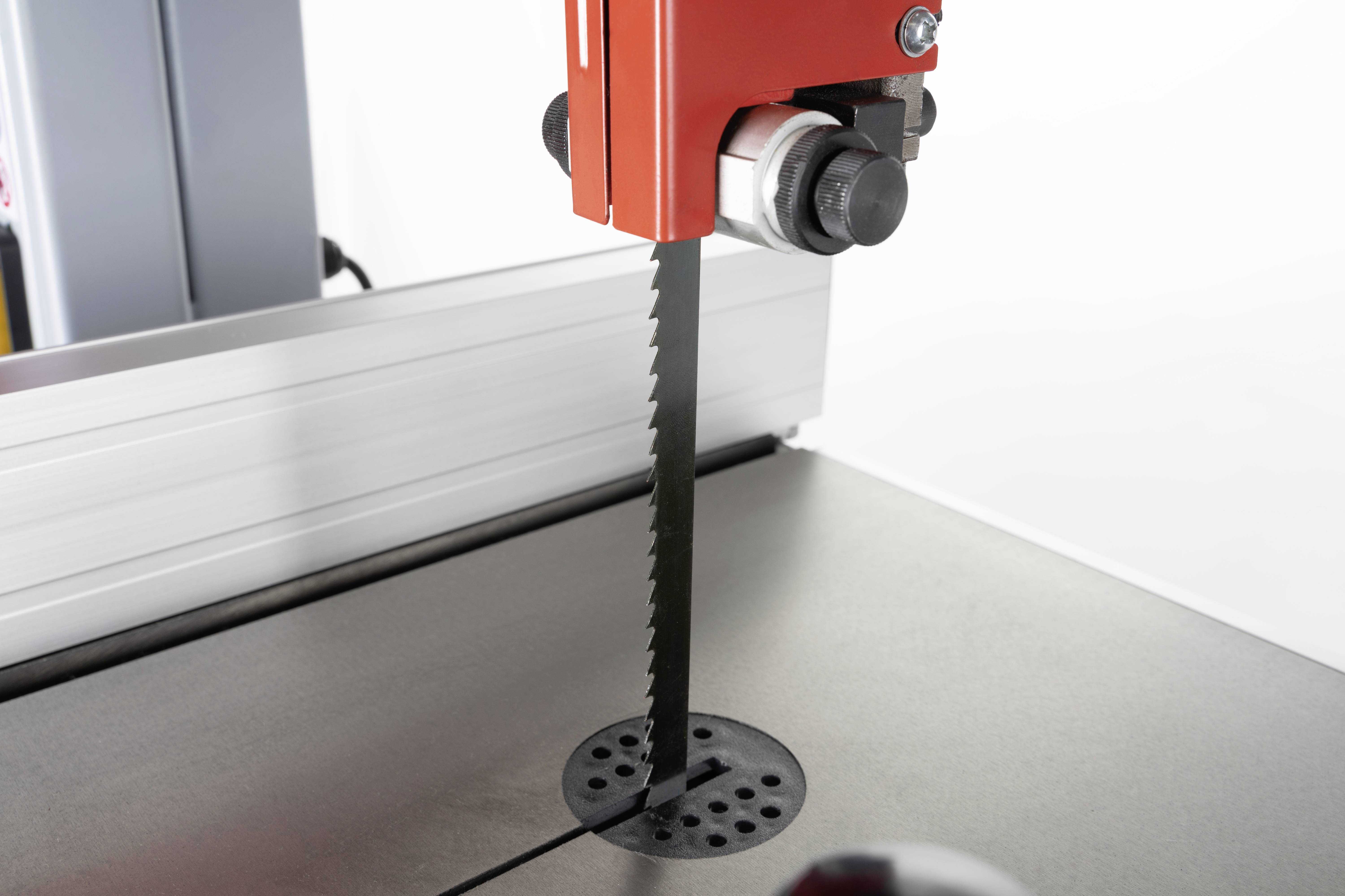 Piła taśmowa z ząbkowanym ostrzem, umieszczona na stole w warsztacie. Jest przygotowana do wykonywania prac związanych z cięciem.