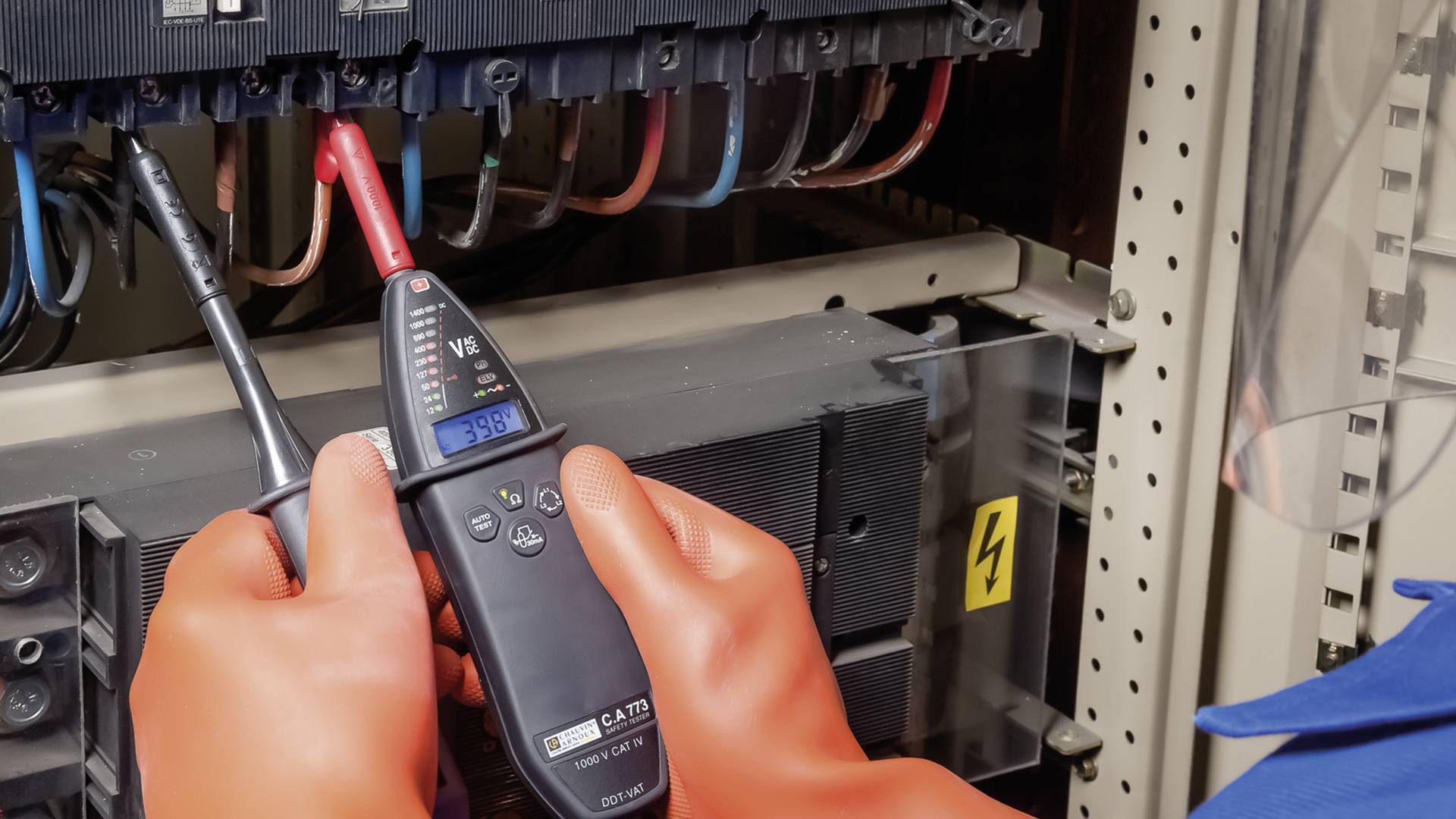 Technik mierzy napięcie w rozdzielni elektrycznej za pomocą multimetru. Ma na sobie rękawice ochronne.