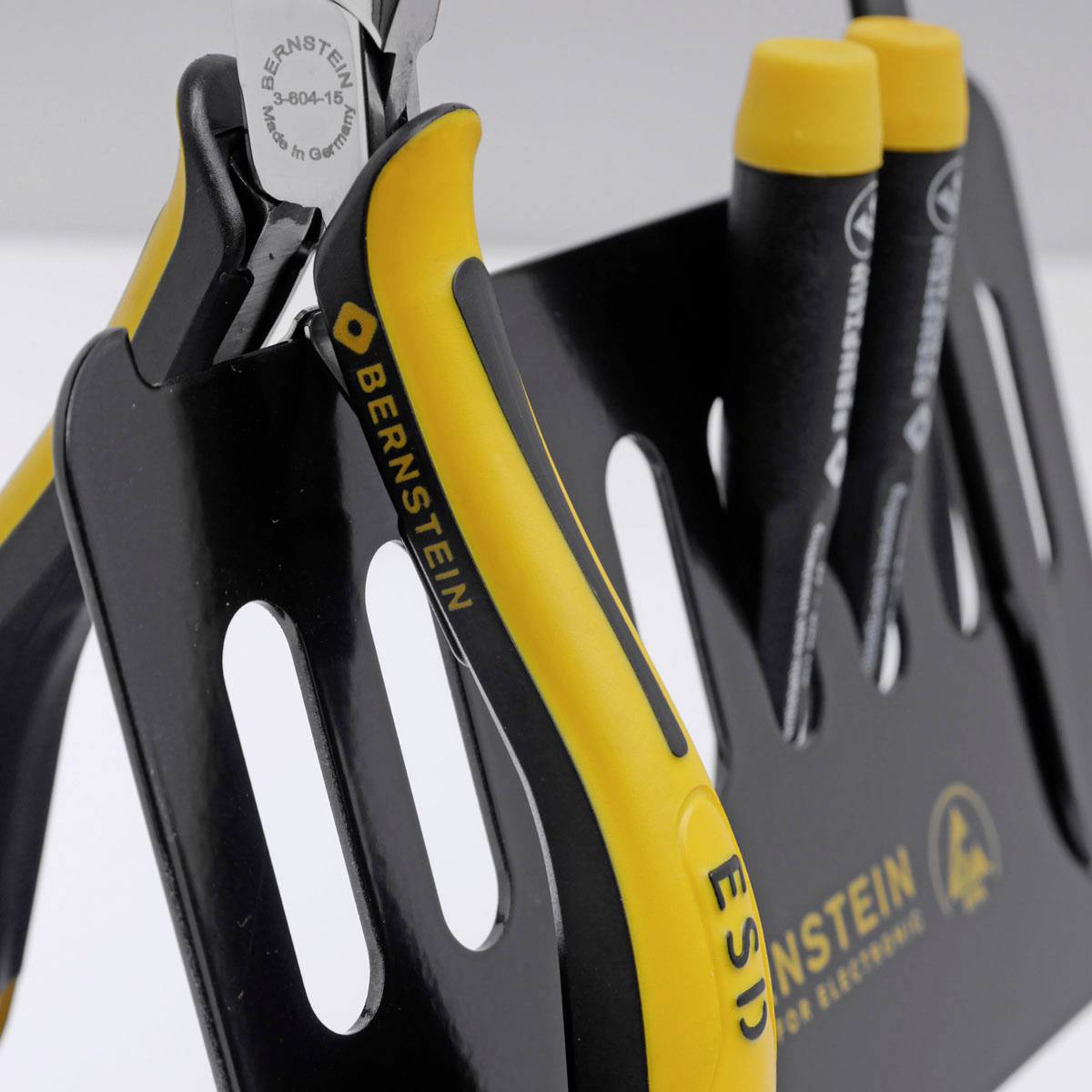 Zbliżenie narzędzi ESD-safe z pomarańczowymi i czarnymi uchwytami w uchwycie Bernsteina, prezentujące szczypce i wkrętaki do precyzyjnych prac.