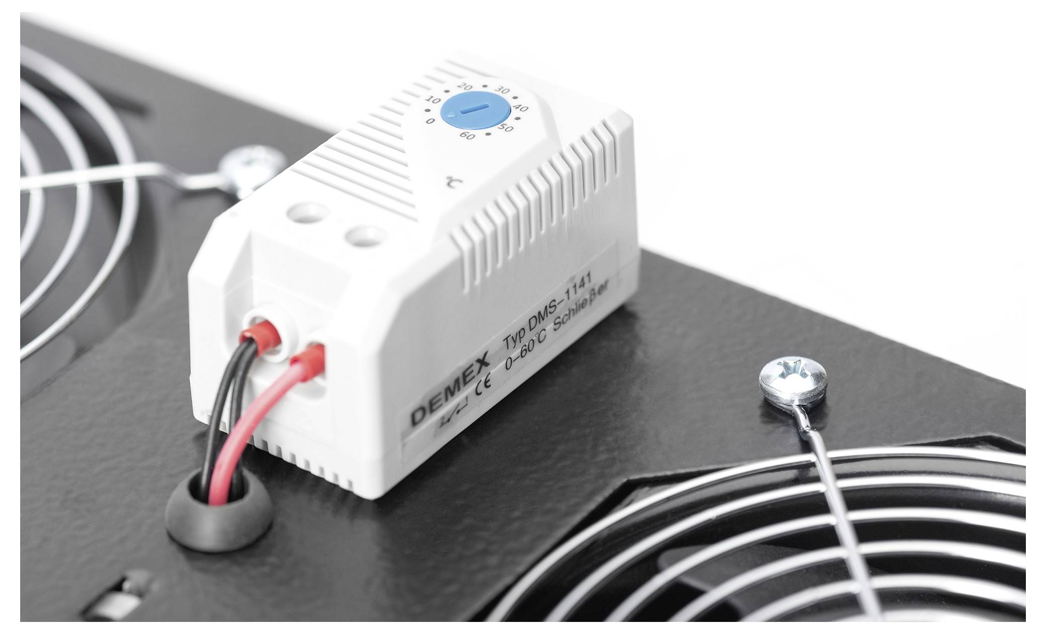 Białe urządzenie termostatu z niebieskim pokrętłem zainstalowane na czarnej powierzchni blisko wentylatora chłodzącego, podłączone przewody. Używane do kontroli temperatury.