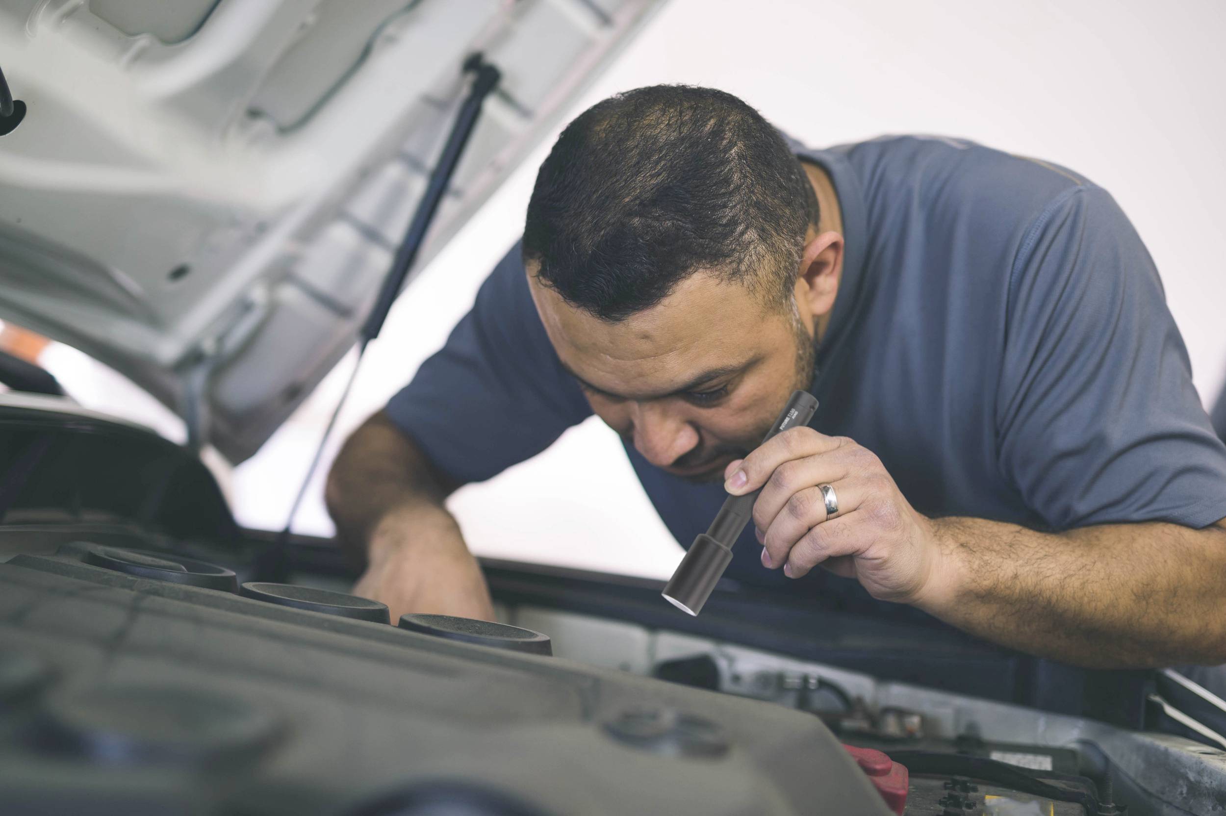 Mechanik sprawdza silnik pod otwartą maską samochodu, używając latarki, aby mieć lepszą widoczność.