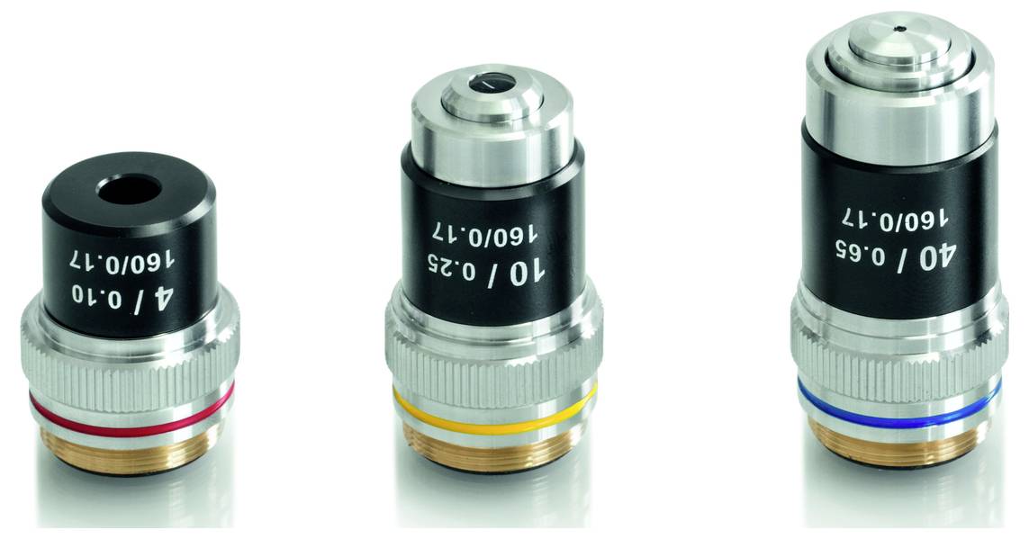 Trzy obiektywy mikroskopowe o różnych powiększeniach i kolorowych oznaczeniach stoją obok siebie na powierzchni odbijającej światło.