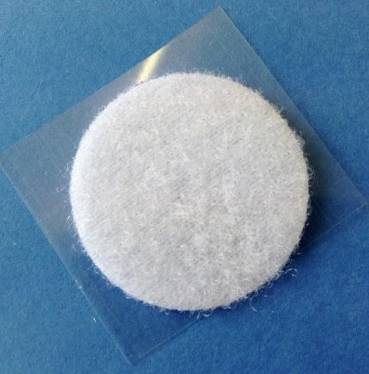 Biała podkładka filcowa na niebieskim tle, prawdopodobnie pad czyszczący lub samoprzylepny kawałek filcu do mebli.