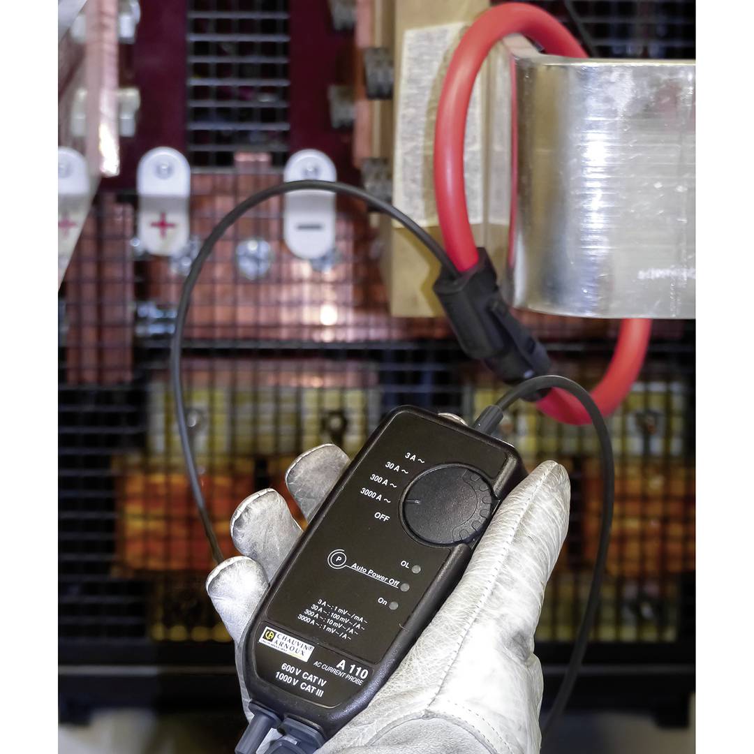 Ręka trzyma miernik prądu przy przewodzie w elektrycznej szafce rozdzielczej