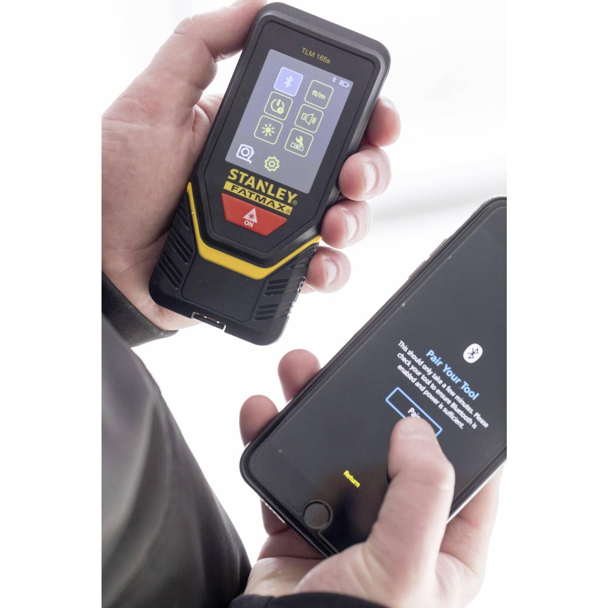 Osoba trzyma dalmierz i smartfon, który jest połączony z urządzeniem pomiarowym, aby wyświetlać i synchronizować dane.