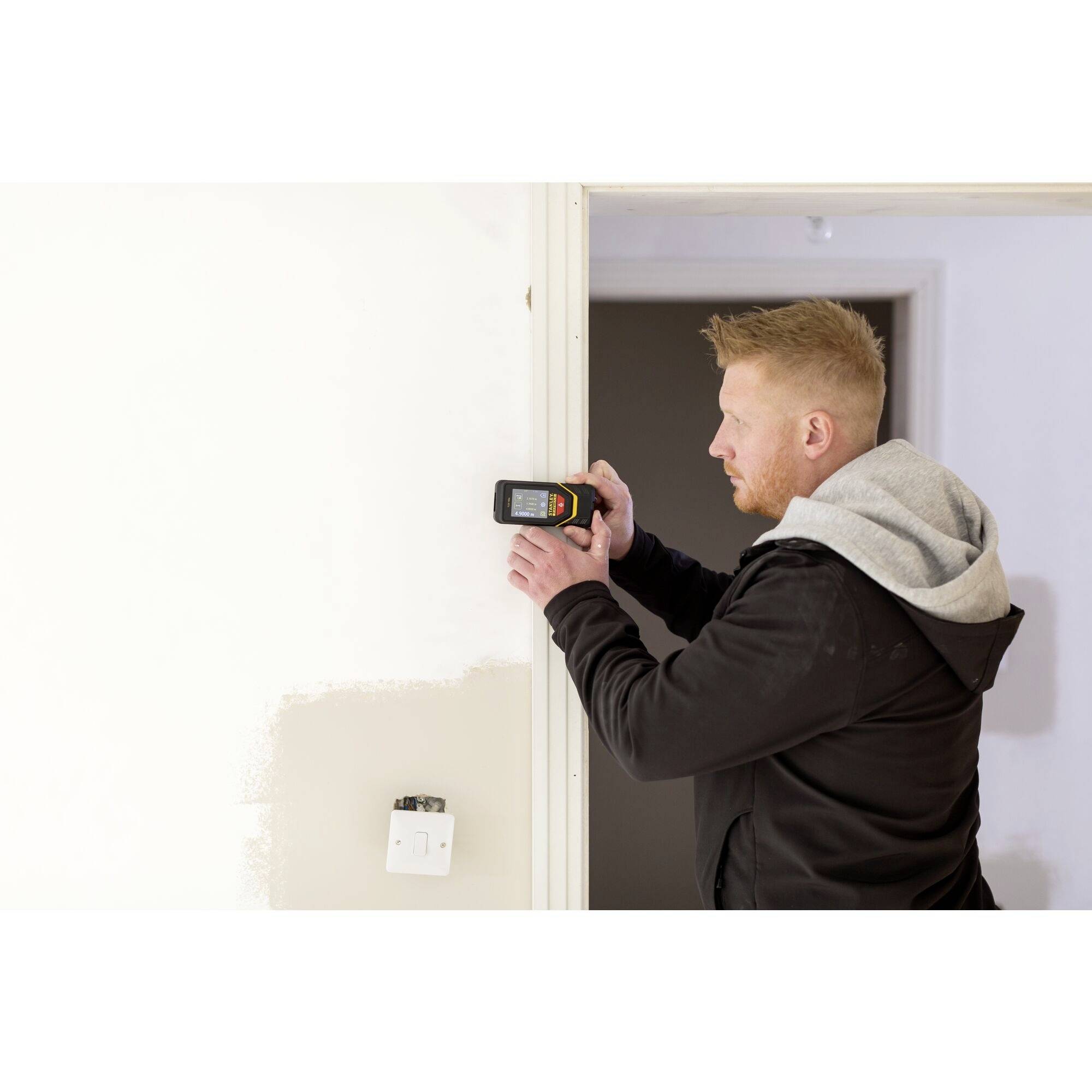 Mężczyzna używa elektronicznego urządzenia pomiarowego przy framudze drzwi, aby przeprowadzić pomiary.