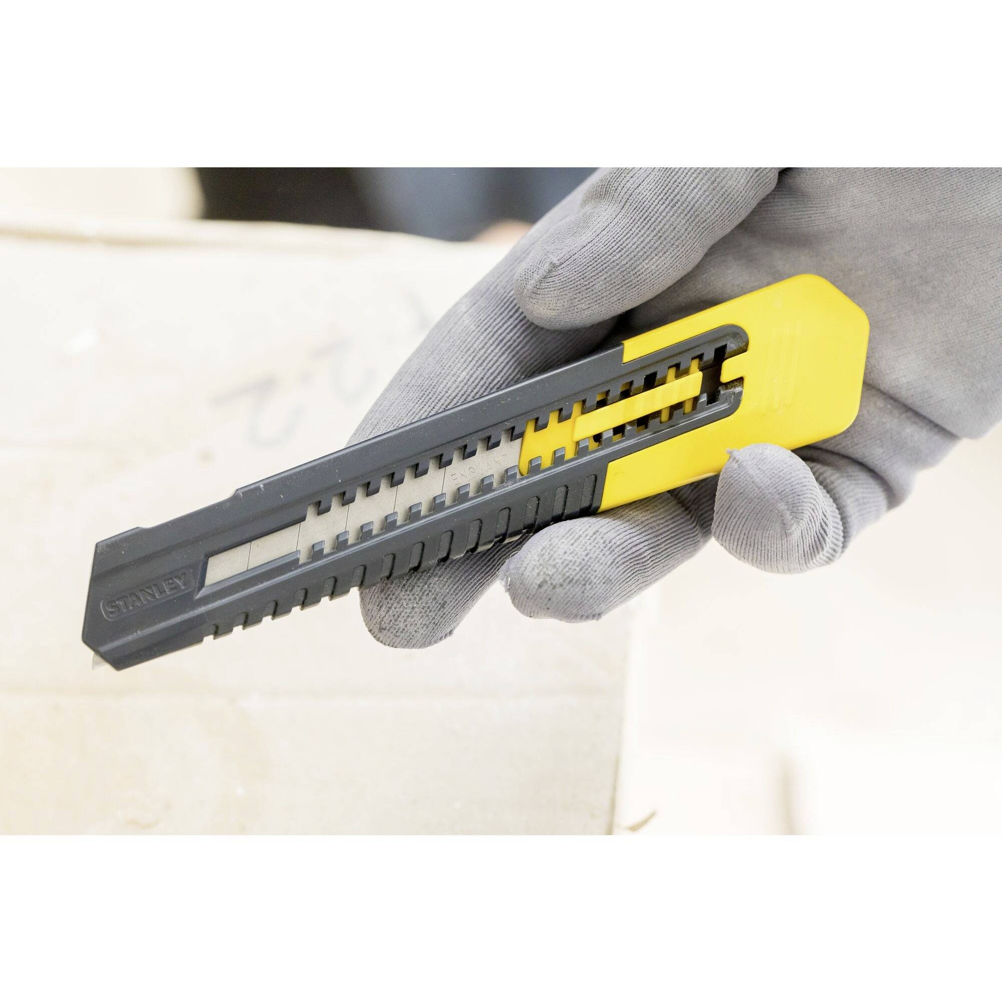 Dłoń w szarej rękawiczce trzyma żółto-czarny nóż do tapet.