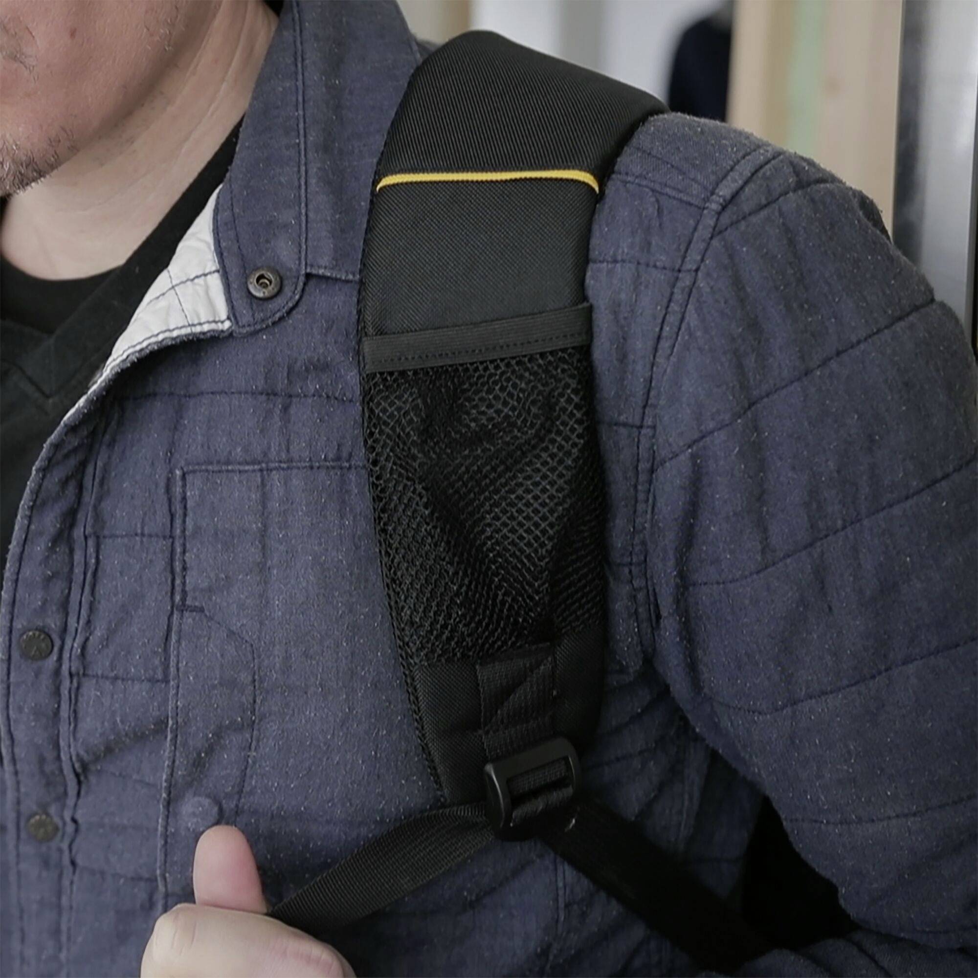 Osoba nosi ciemnoniebieską kurtkę i czarny plecak. Pasek plecaka jest wyraźnie widoczny na ramieniu.