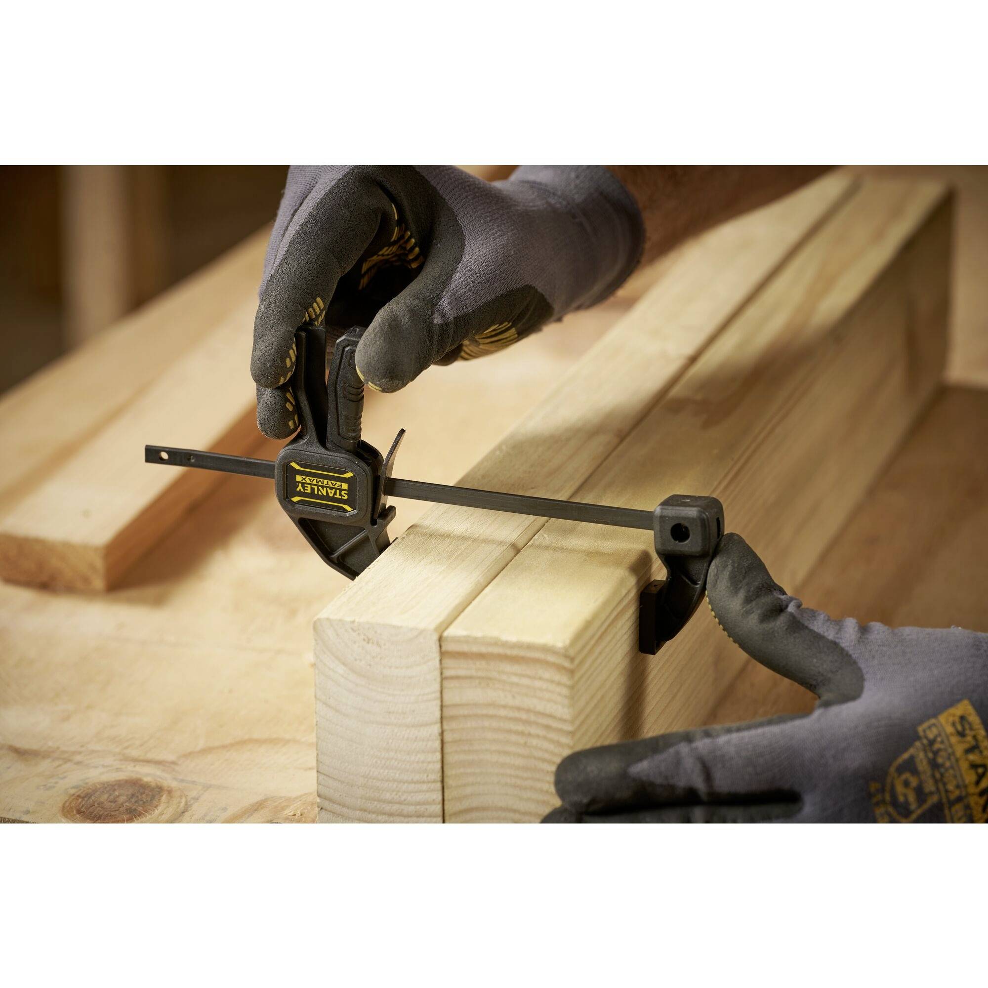 Osoba dokładnie mierzy odległość między dwoma kawałkami drewna za pomocą miarki. Scena przedstawia precyzyjną pracę rzemieślniczą.