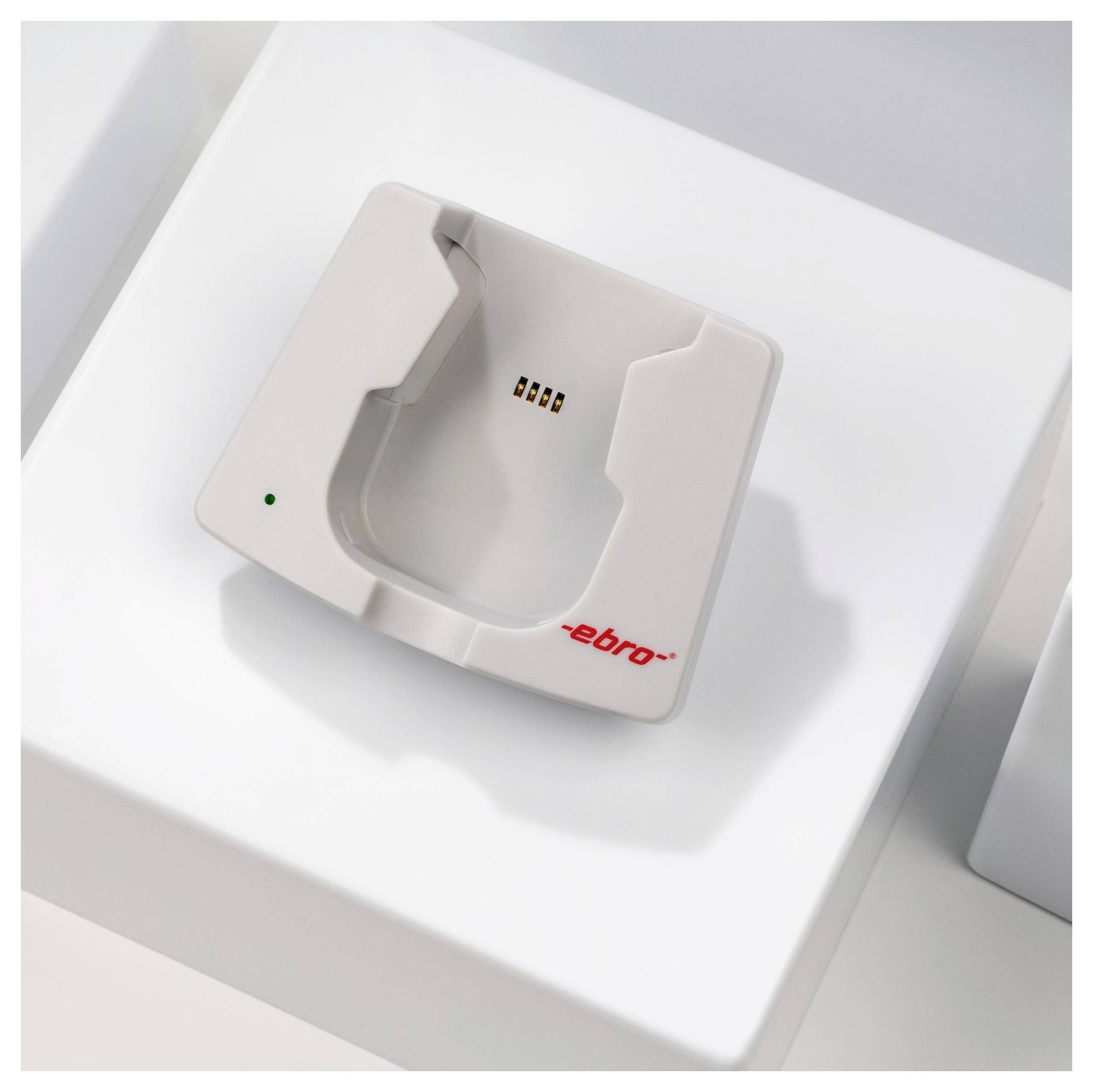 Stacja dokująca do urządzenia 'Ebro', wyposażona w złącze pinowe i zielony wskaźnik oświetlenia, umieszczona na białej powierzchni.