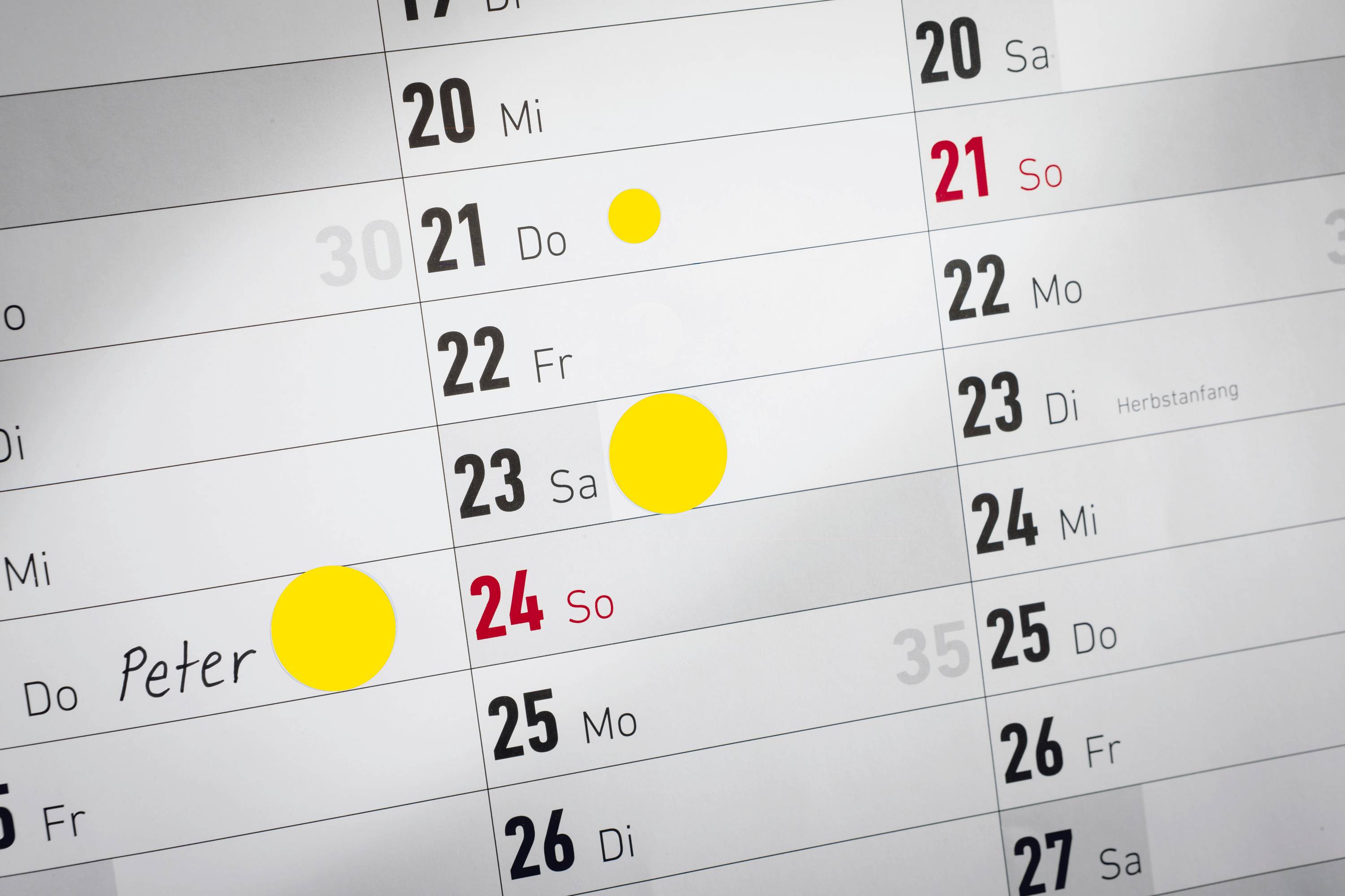 Widok kalendarza z zaznaczonymi żółtymi punktami 20., 21., 23. i 24 października; ręcznie napisane 'Piotr' przy dacie 24 października.