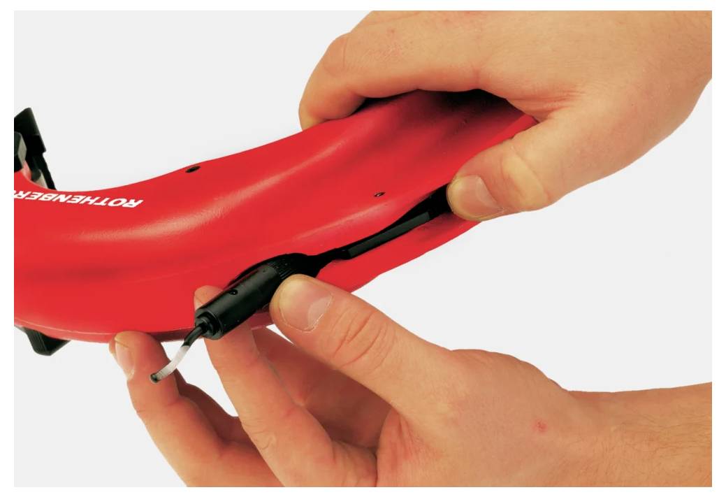 Ilustracja „Wkładanie gumowego uszczelnienia w celu zakrycia portu ładowania" pokazuje ręce instalujące ochronne uszczelnienie w czerwonym urządzeniu plastikowym.