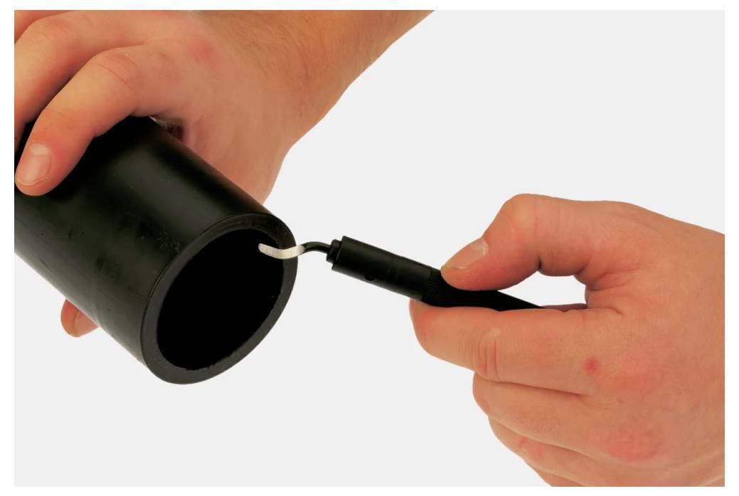 'Ręce demonstrujące usuwanie ostrych krawędzi czarnej rury za pomocą narzędzia; pokazujące proces wygładzania wewnętrznej krawędzi rury.'