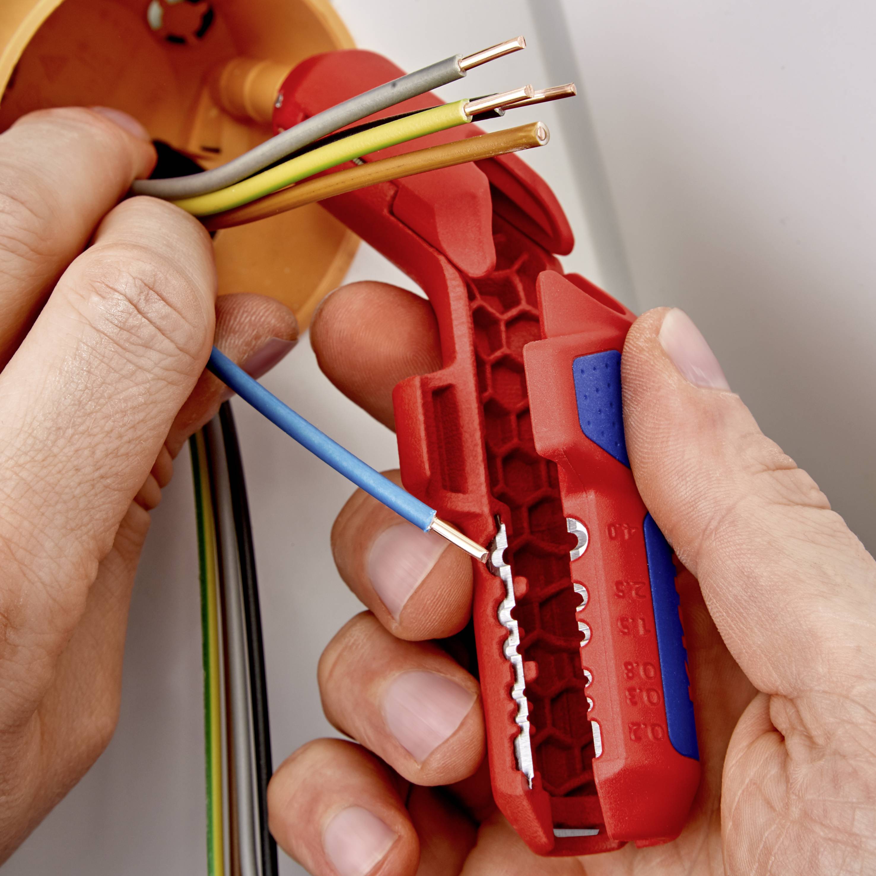 Osoba trzyma narzędzie do zdejmowania izolacji i usuwa izolację z niebieskiego przewodu, odsłaniając jego wnętrze.