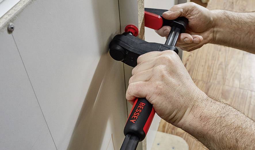 Dwie ręce używają zacisku, aby mocno połączyć dwie części drewna. W tle drewniana podłoga.