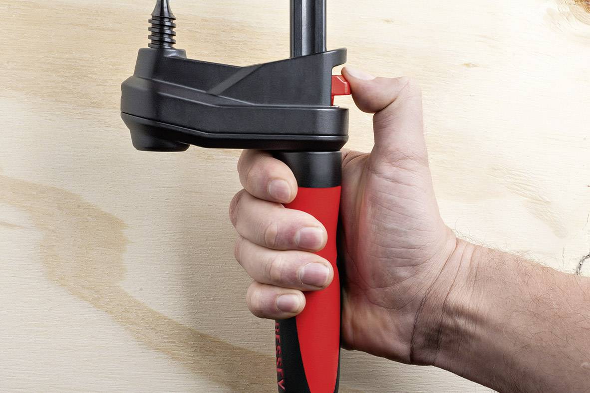 Dłoń trzyma czerwony i czarny zacisk przy drewnianej powierzchni.