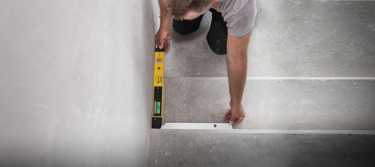 Osoba sprawdza poziom schodów za pomocą poziomicy, aby ocenić ich prawidłowe wypoziomowanie.