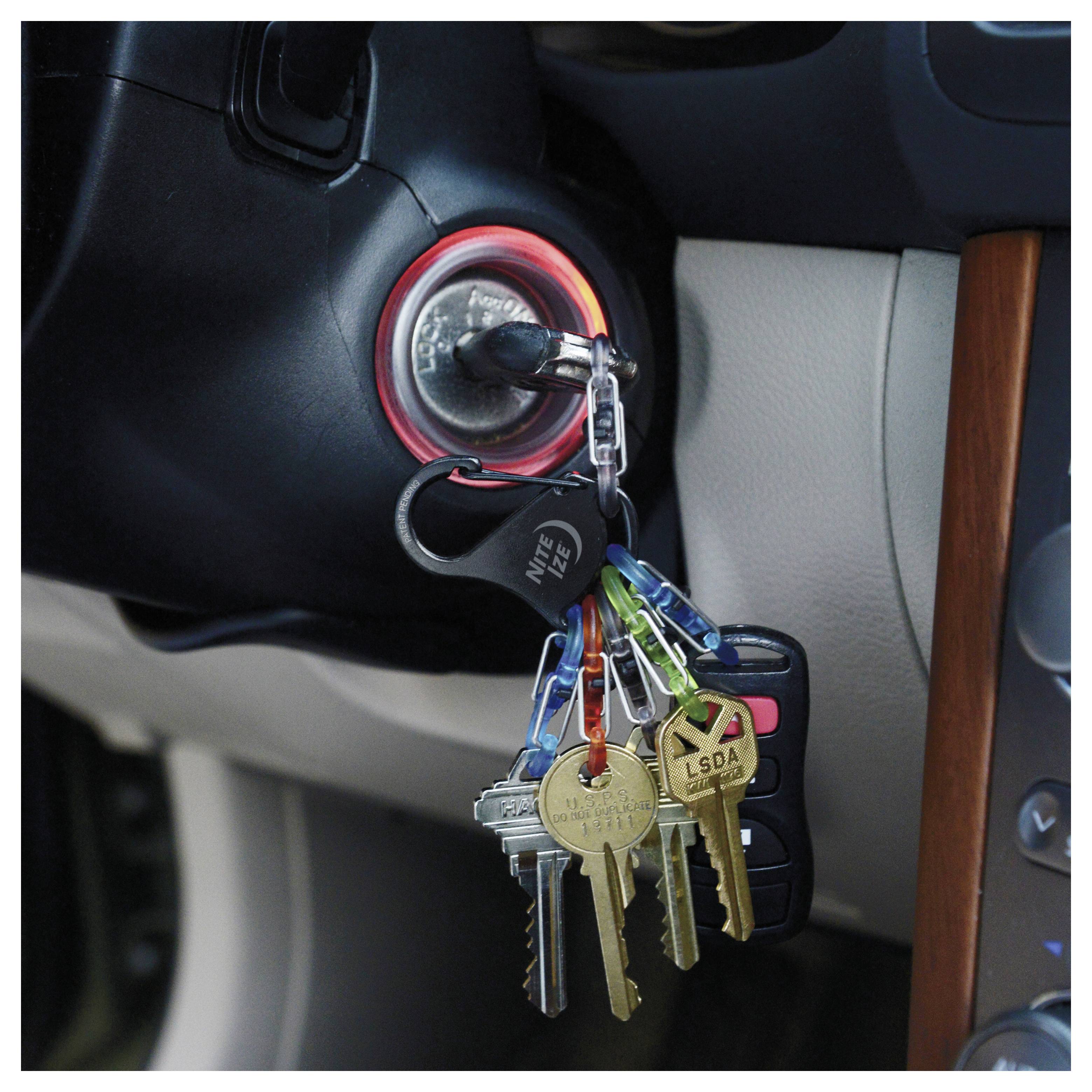 Zestaw kluczyków samochodowych z srebrnym breloczkiem w stacyjce pojazdu, otoczony różnymi innymi kluczami i pilotem, sugerujący, że samochód jest gotowy do uruchomienia.