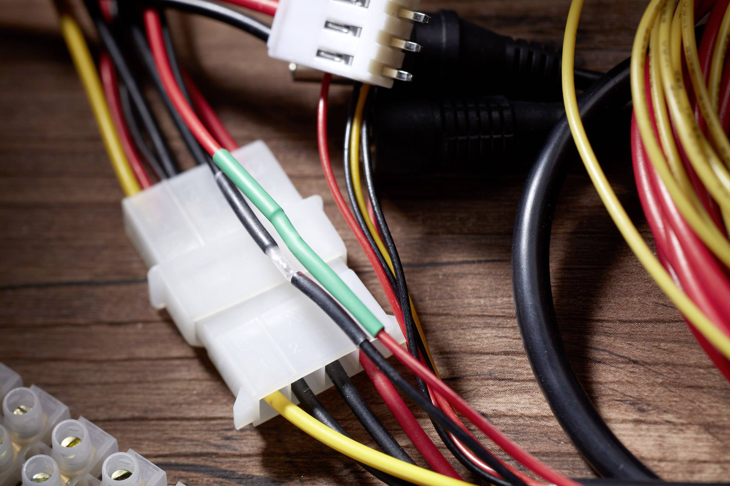 Wielokolorowe przewody przymocowane do białej wtyczki leżą na drewnianej powierzchni. Akcesoria elektroniczne.