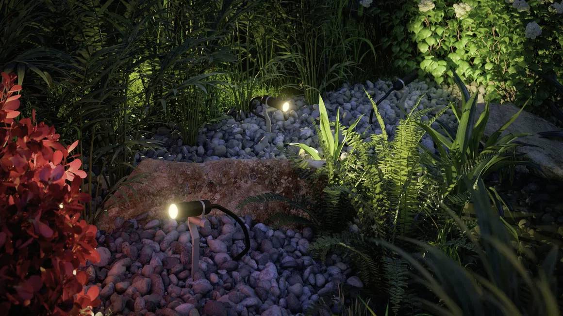 Oświetlenie ogrodu nocą: Trzy reflektory rozświetlają skalniak, otoczony gęstą roślinnością. Podkreśla naturalne tekstury i różnorodność roślin.