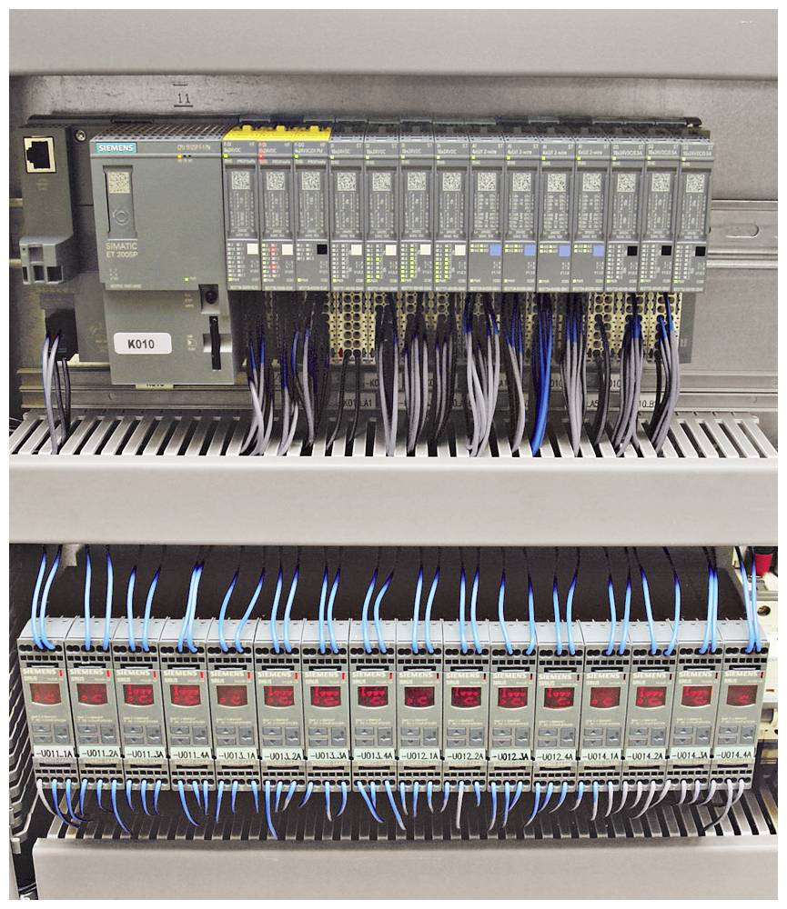 Szafa sterownicza z wieloma modułami elektronicznymi i połączeniami kablowymi; przedstawia złożony system do sterowania procesami technicznymi.